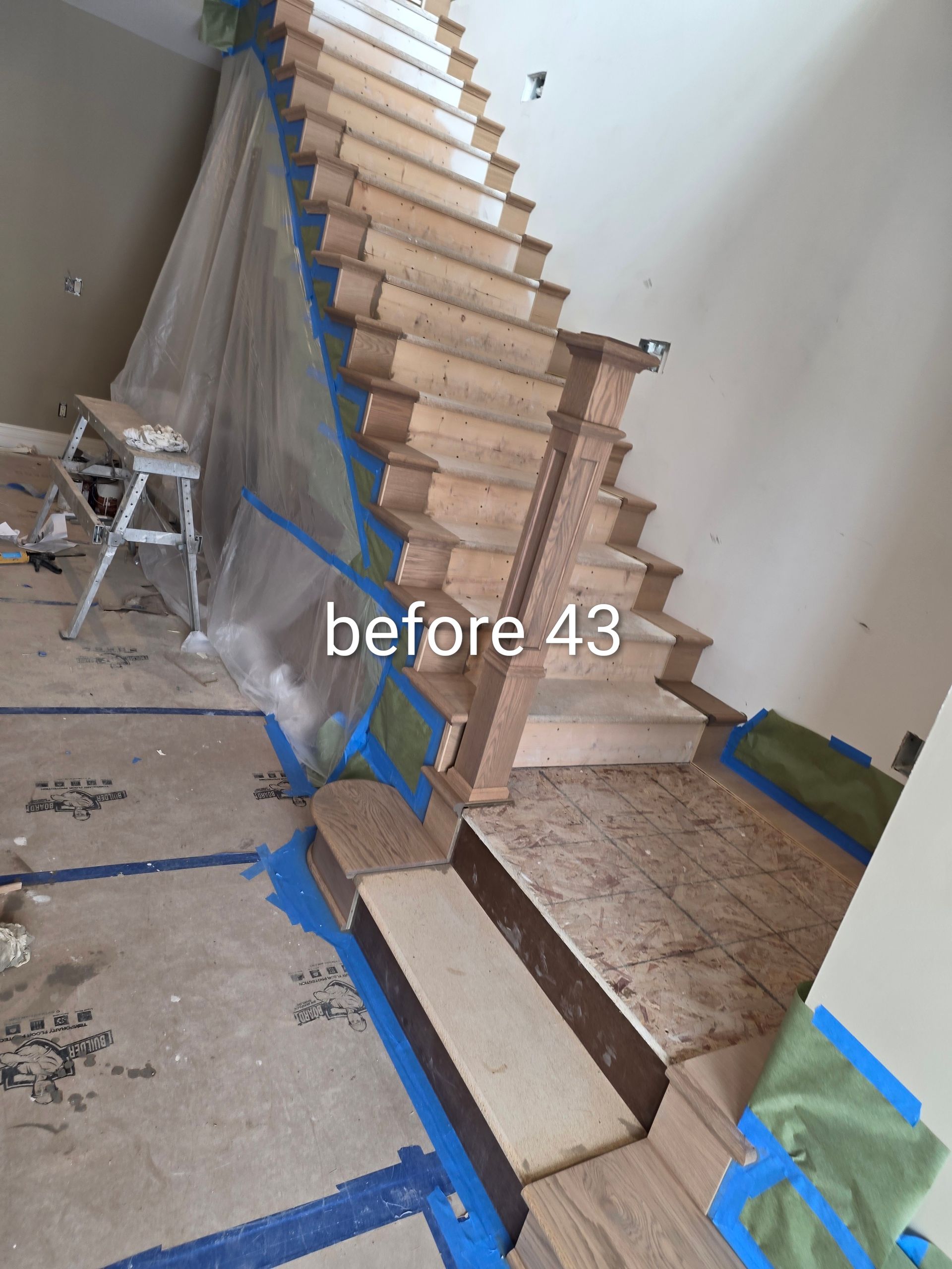 Interior stair under construction, with taped floor and unfinished wooden steps along a wall.