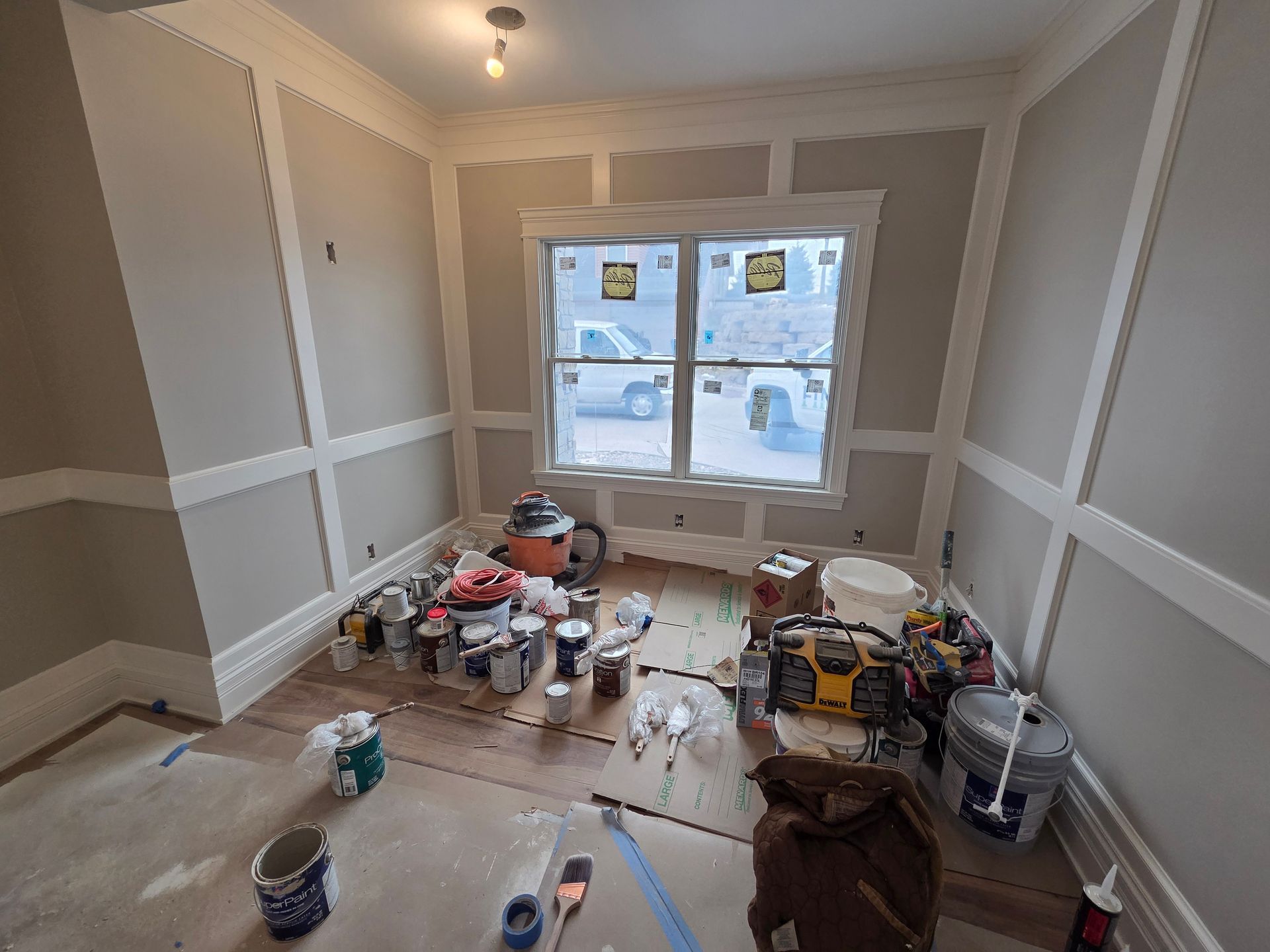 Unfinished room with painting supplies, plastic-covered floor, and a window overlooking snowy homes.