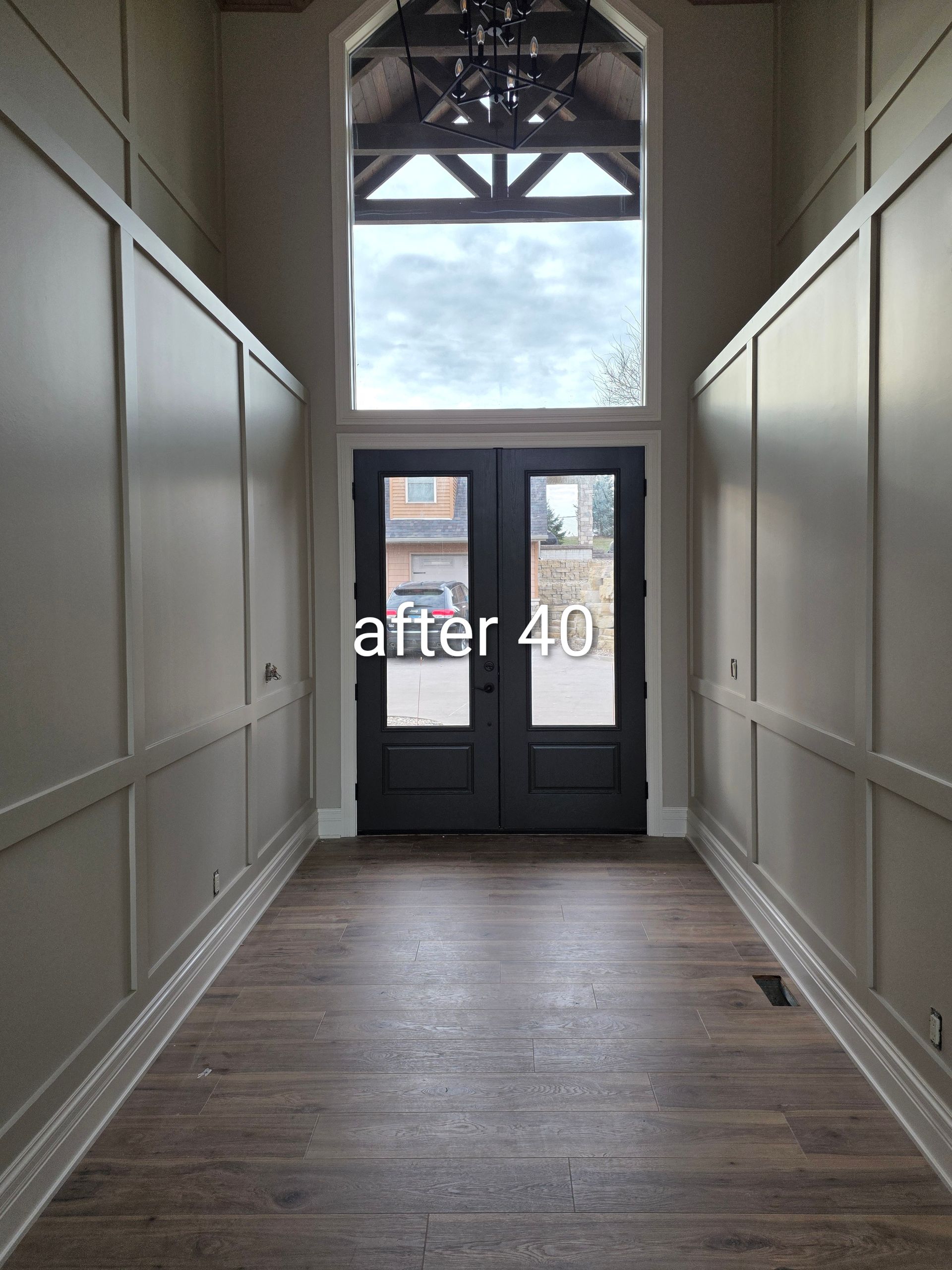Empty hallway with white paneled walls and dark wood floors, leading to glass double doors at the end.