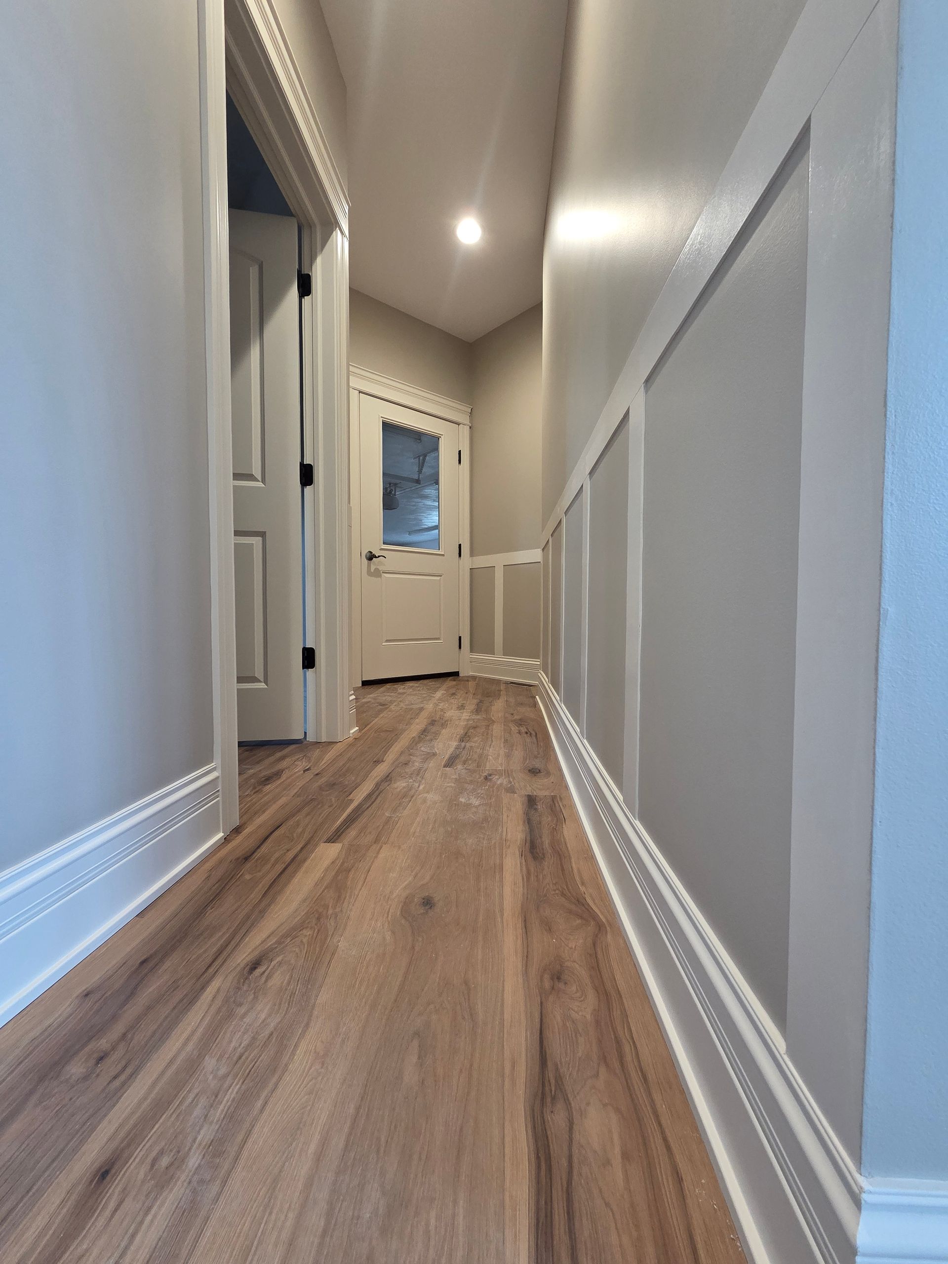 Narrow hallway with wood floors, white walls, and a door at the end.