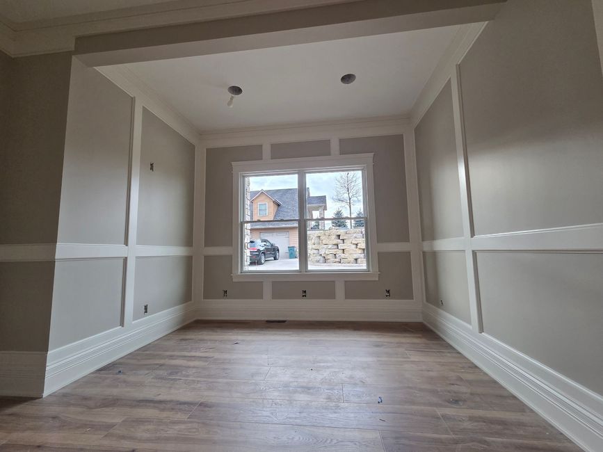 Empty beige room with wood floors, white trim, and a window at the far end.
