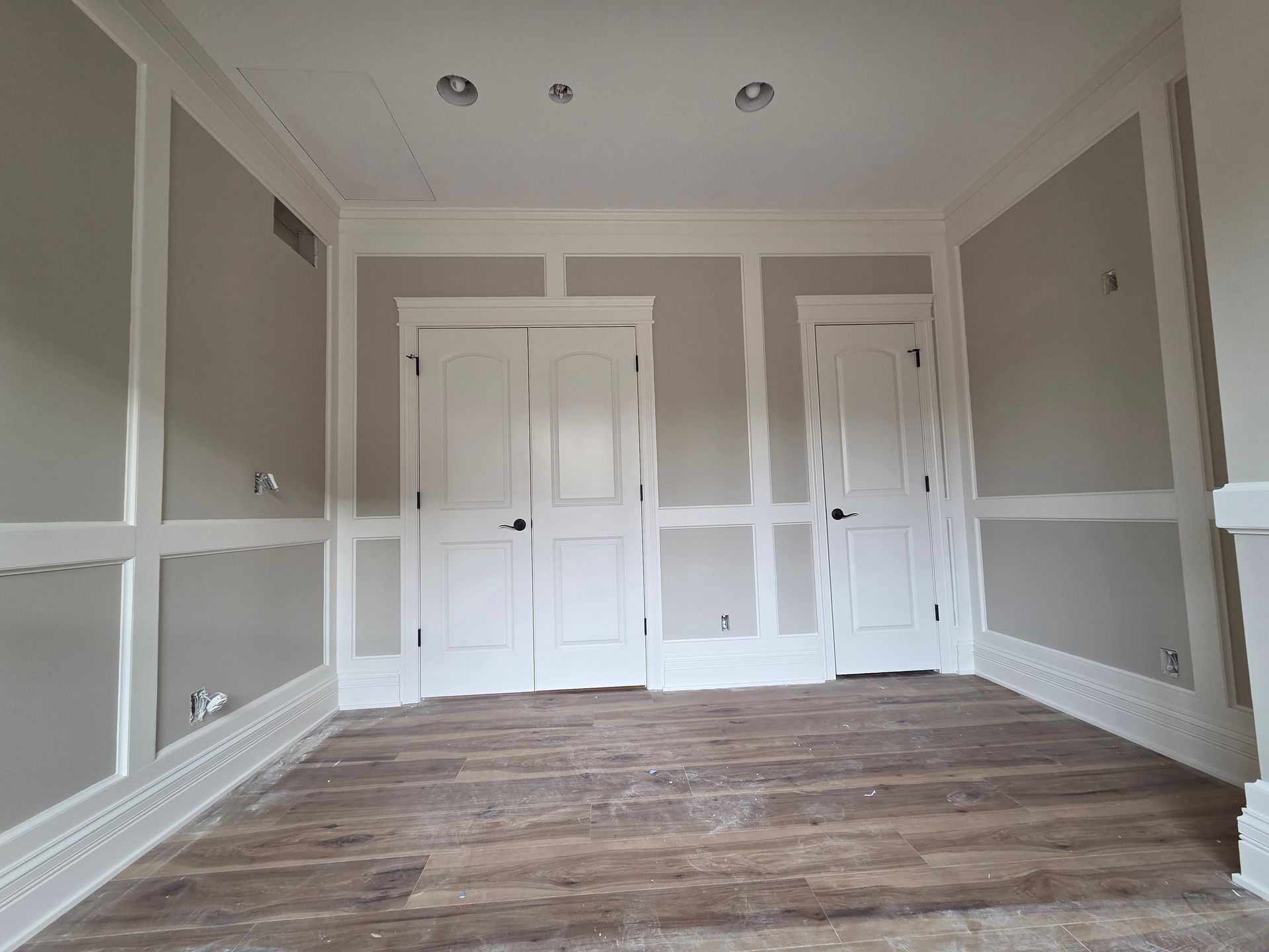 Empty room with gray walls, white trim, double closet doors, and wood flooring