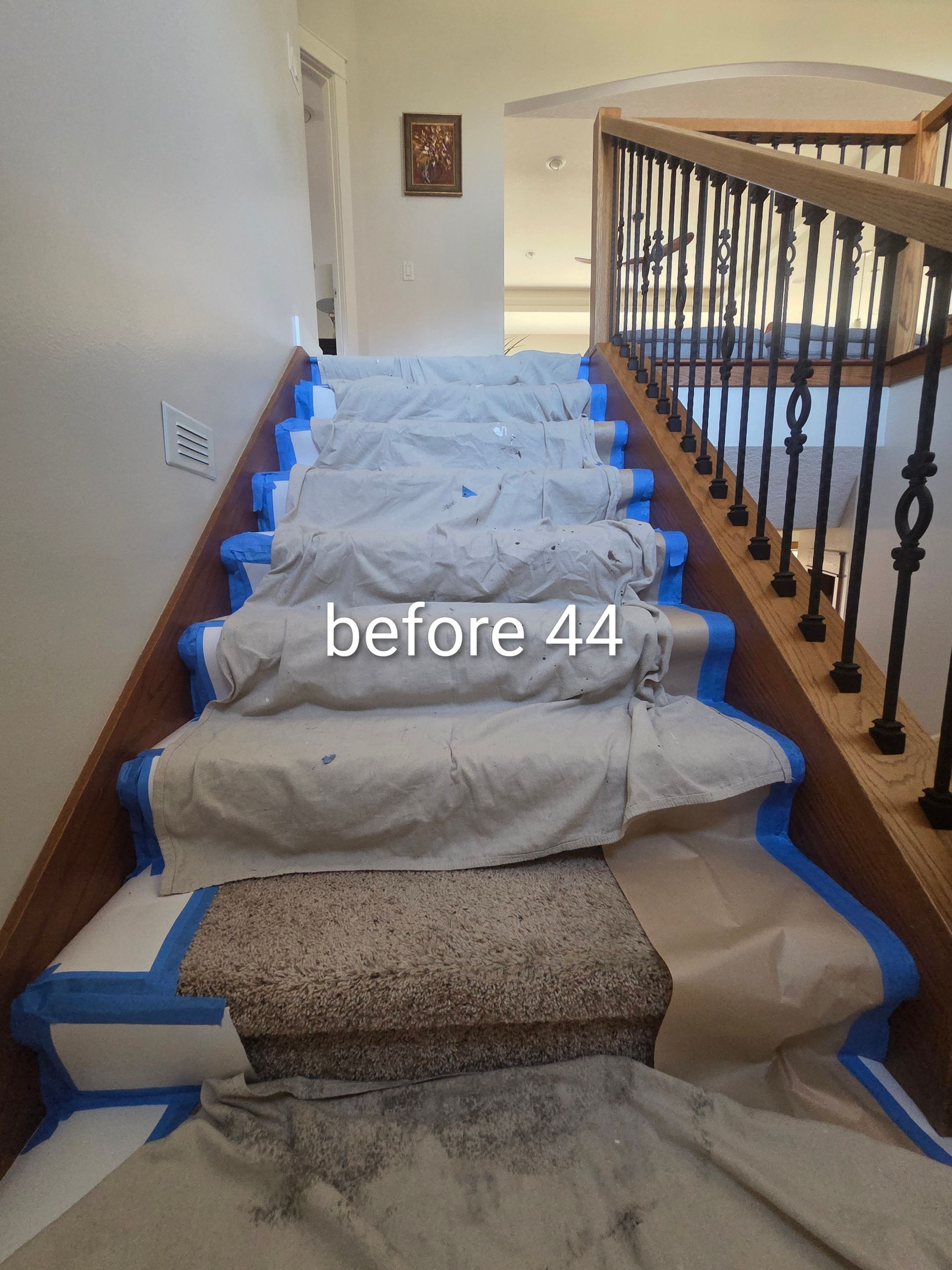 Staircase covered with white protective cloth and blue tape, with carpet exposed at the bottom.