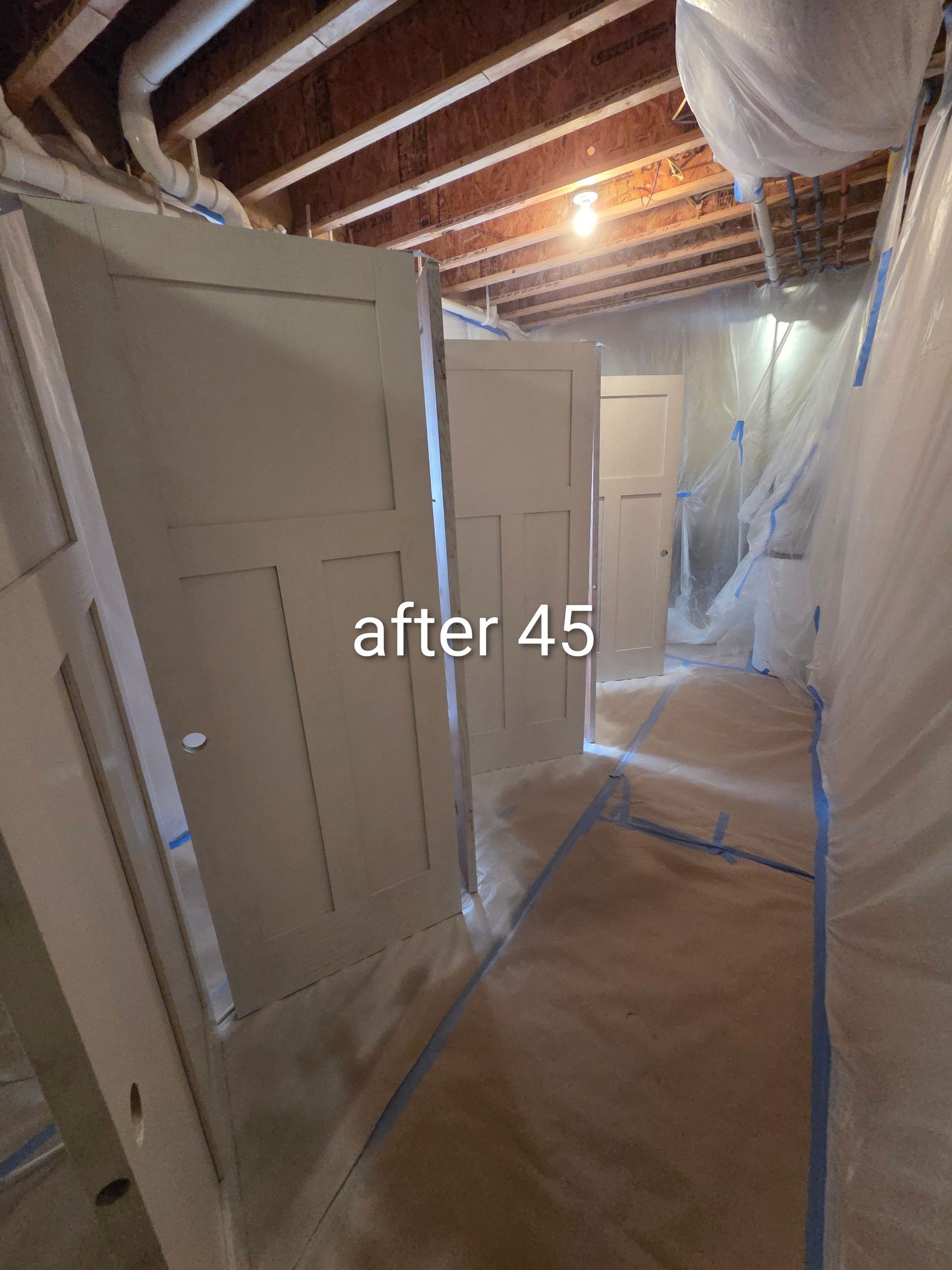 Basement under construction with taped-off white walls, exposed beams, and covered floor; “after 45” text overlay