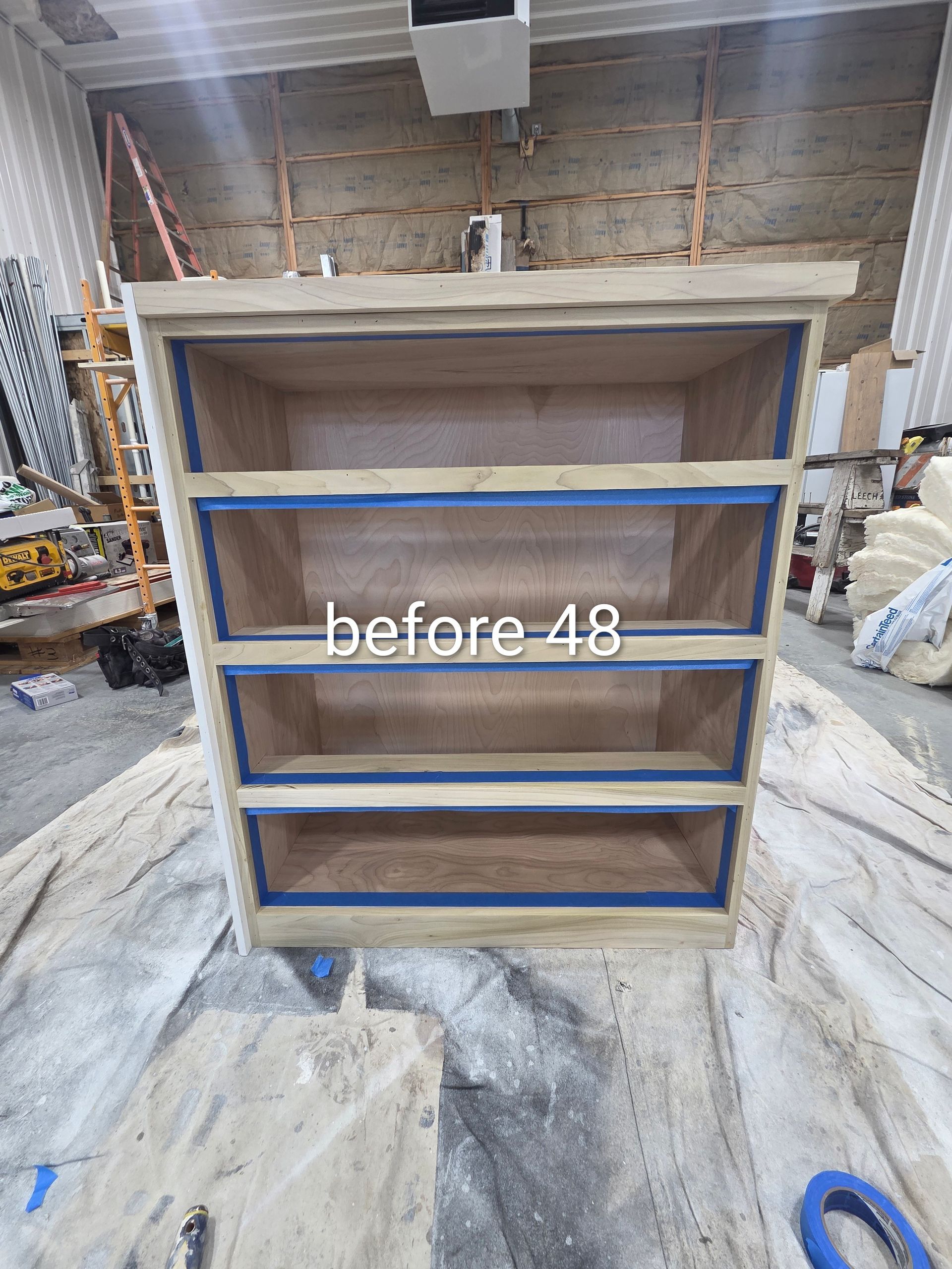Wooden cabinet with blue trim in a workshop, labeled “before 48,” on a dusty floor.