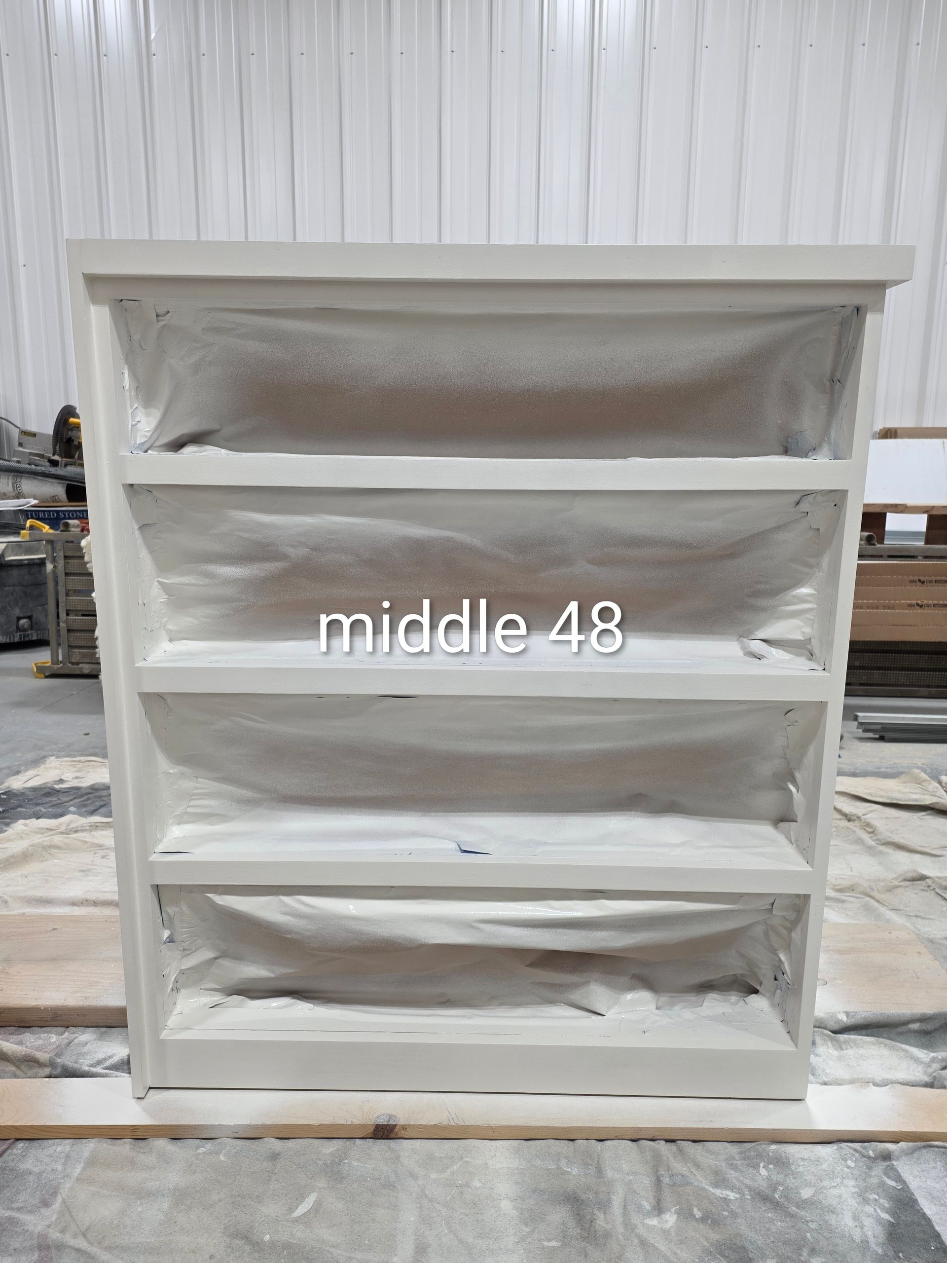 White 4-tier shelving unit in a workshop, with dust covers draped inside each shelf.
