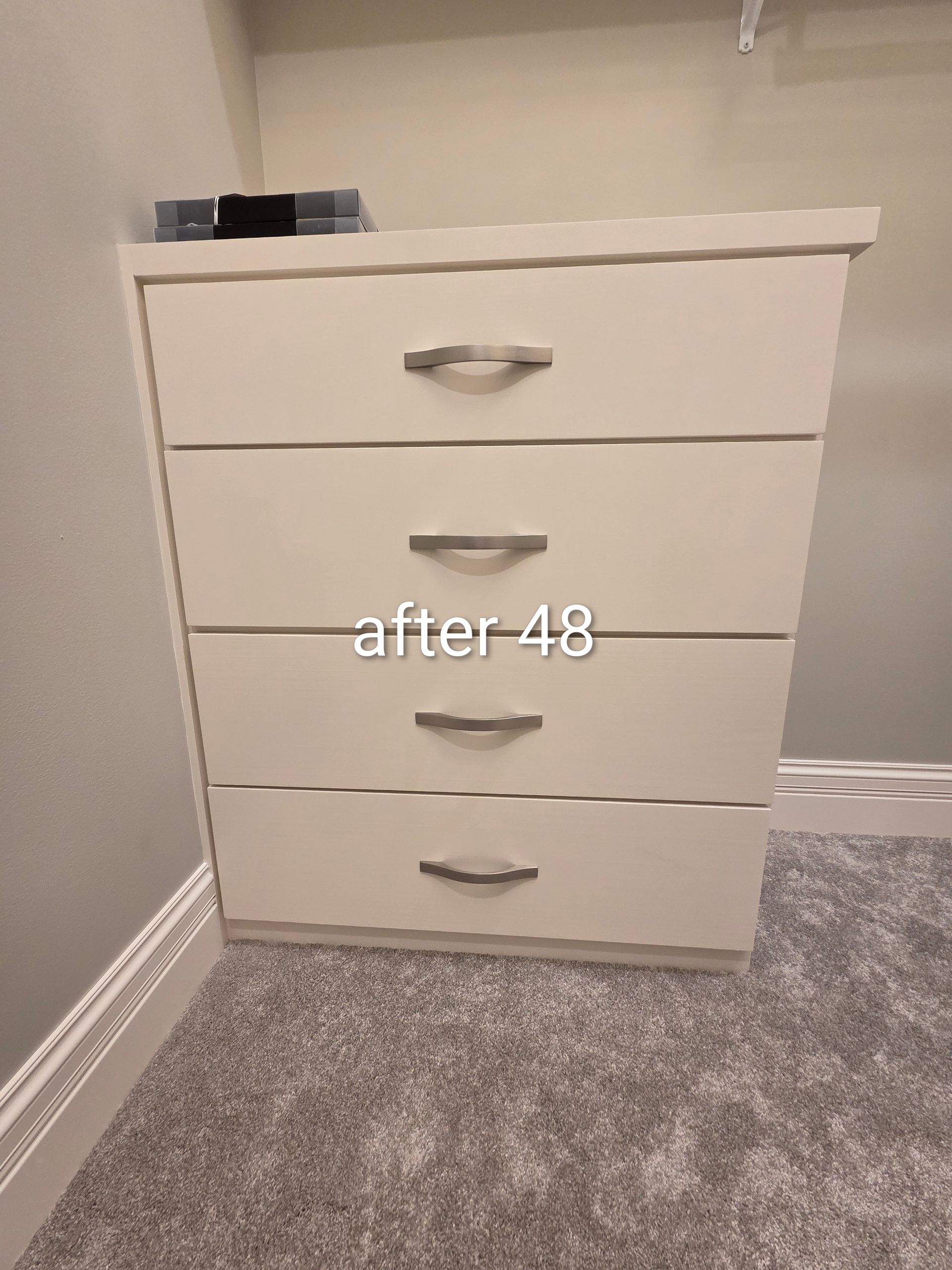White four-drawer dresser in a carpeted room, with a small black object on top.
