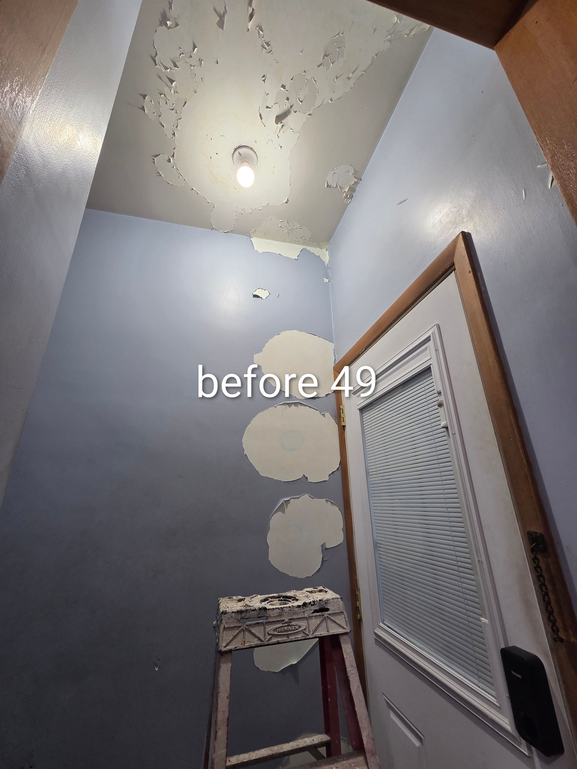Small bathroom with blue walls, ceiling damage, ladder, and patches of plaster repairs near a door