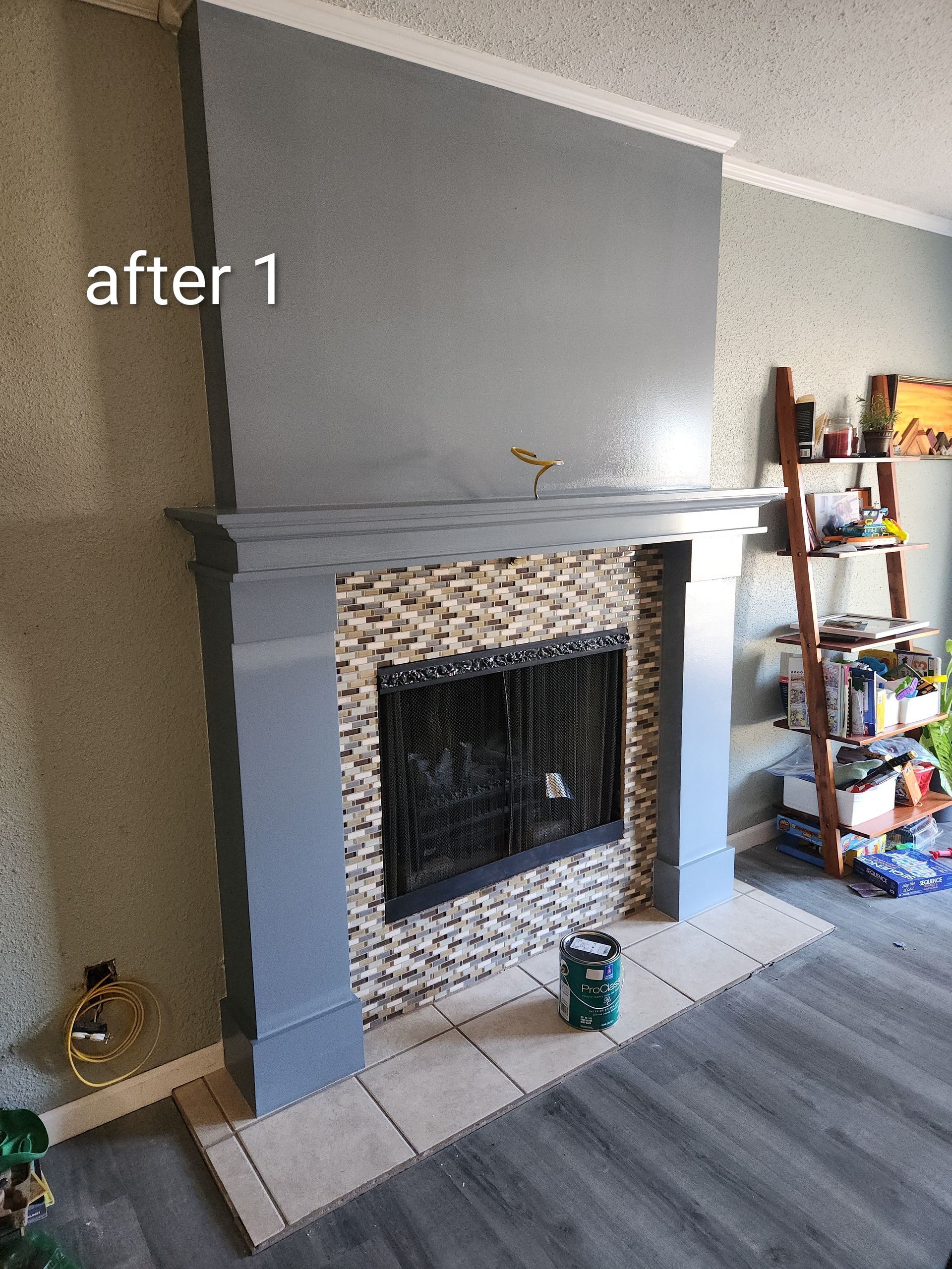 Gray-painted fireplace with tile surround in a living room, beside a carpet and shelving unit.