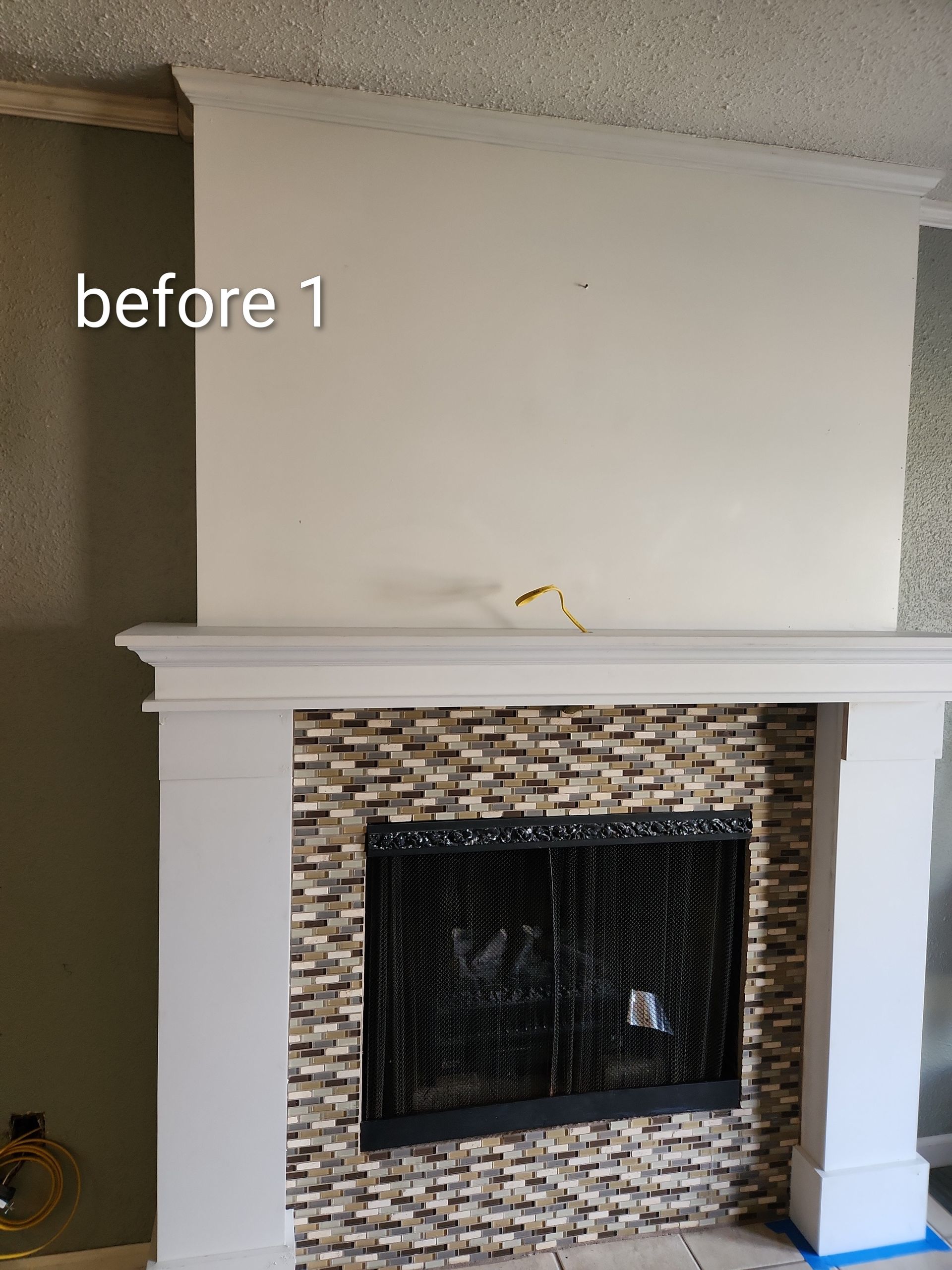 Empty living room fireplace wall with white mantle and mosaic tile surround, labeled “before 1”