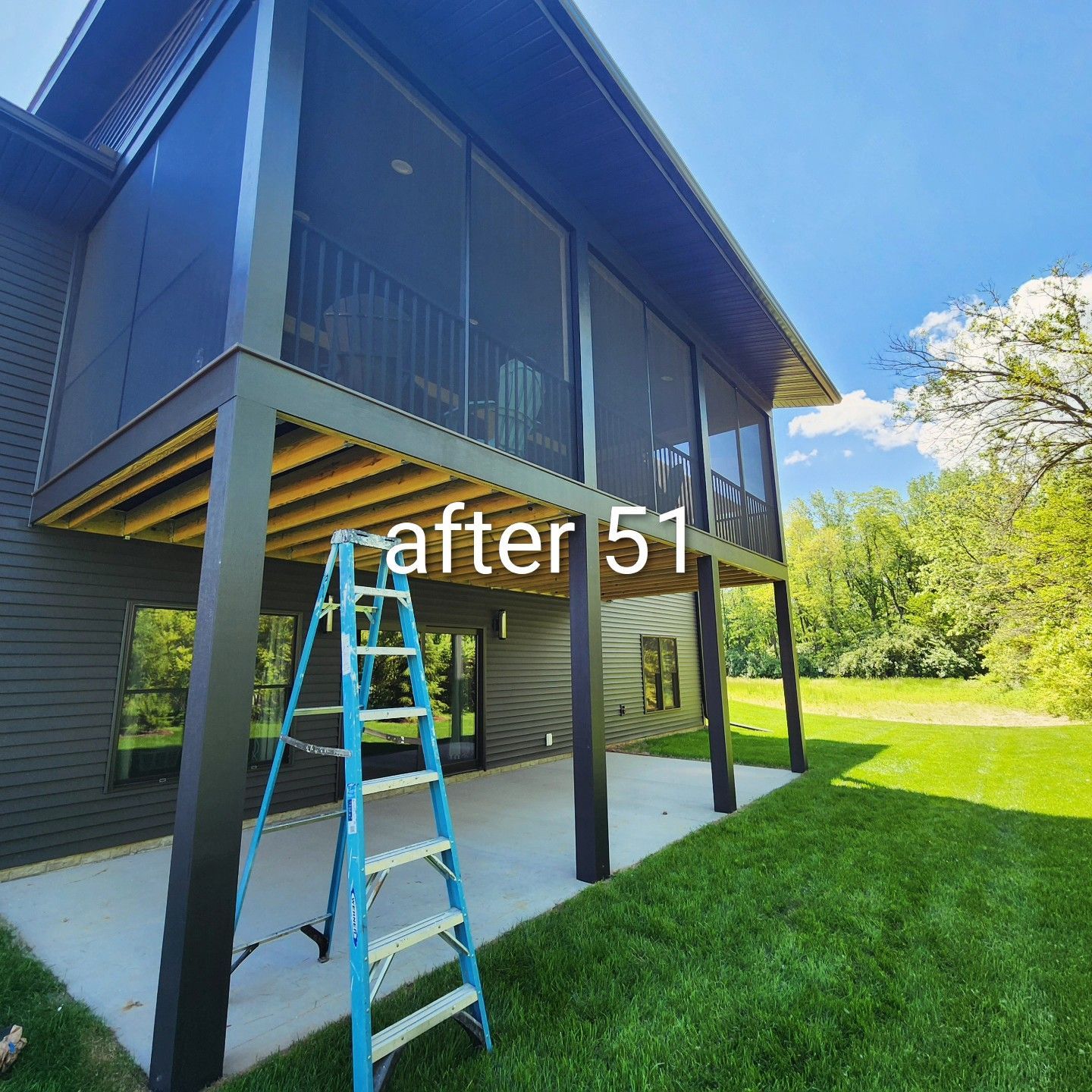Modern black house exterior with screened porch, blue ladder, and green lawn in bright sunlight