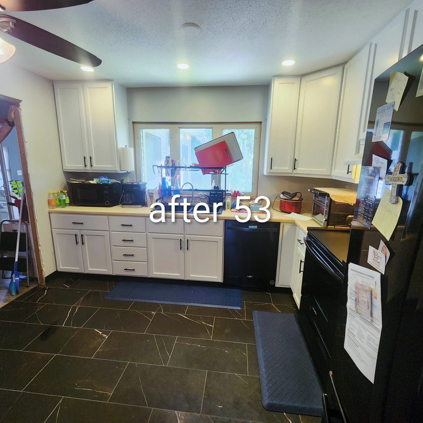 Small kitchen with white cabinets, black tiled floor, and a window above the sink.