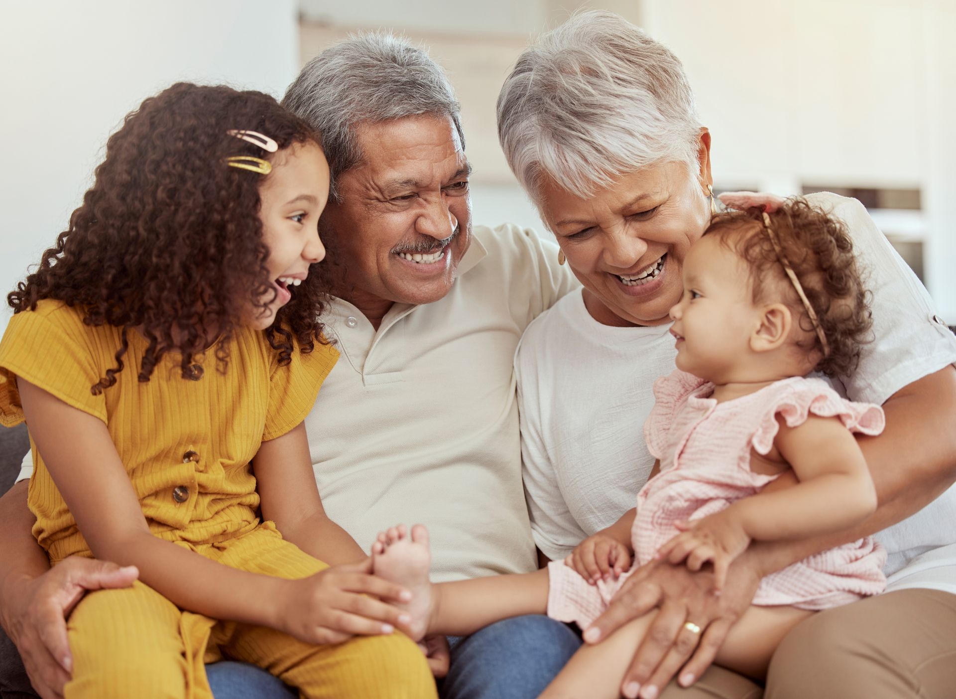Mixed race grandparents enjoying weekend with granddaughters in home living room. Adorable smiling hispanic girls bonding with grandmother and grandfather. Happy seniors and children sitting together stock photo