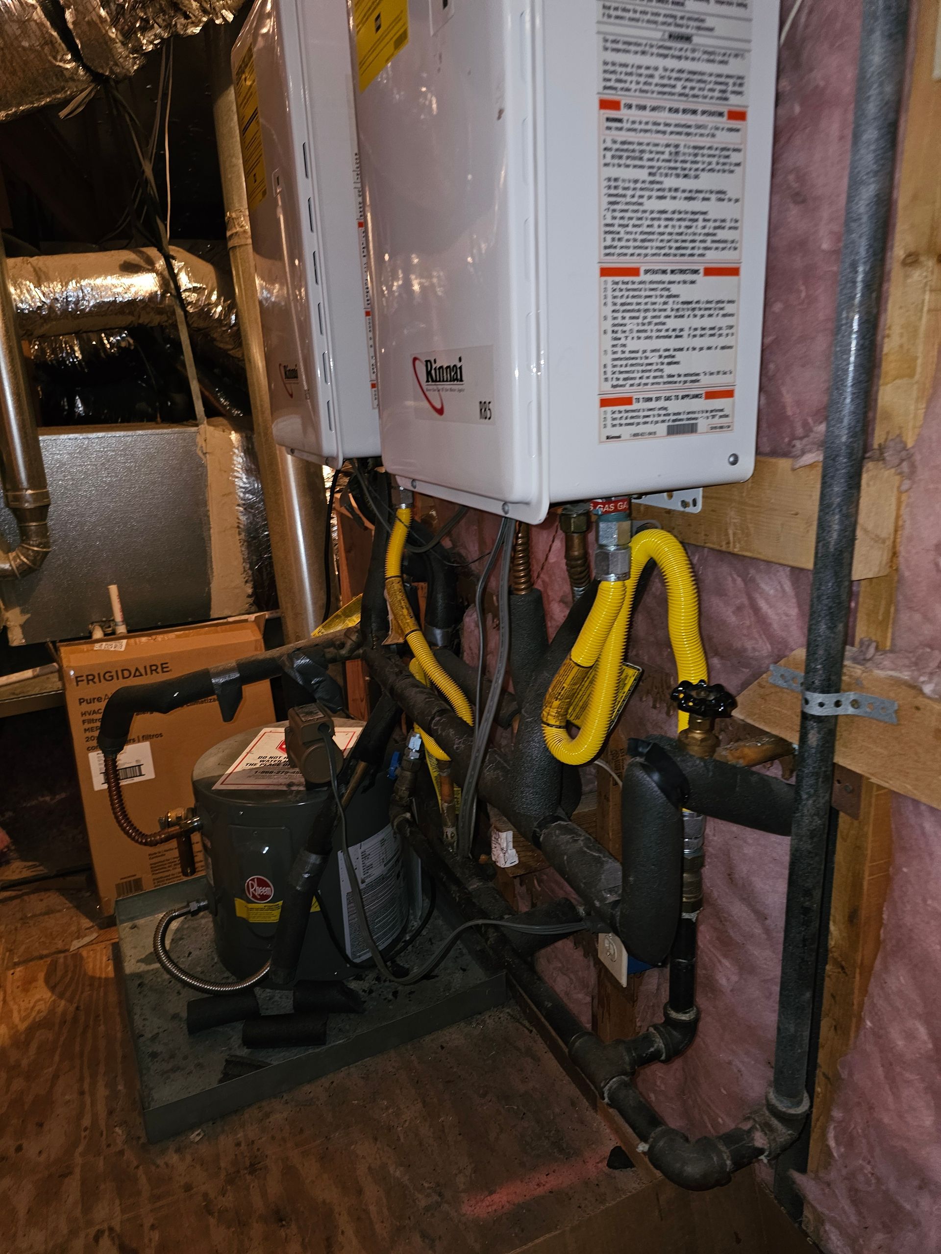 Water heater and pump system with yellow flex lines in a basement, close-up shot.