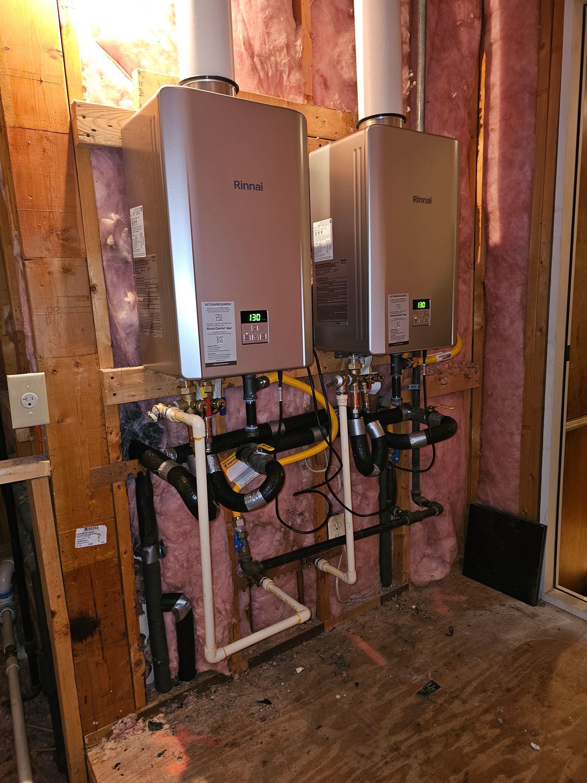 Two water heaters installed on a wooden wall with connected pipes and vent pipes.