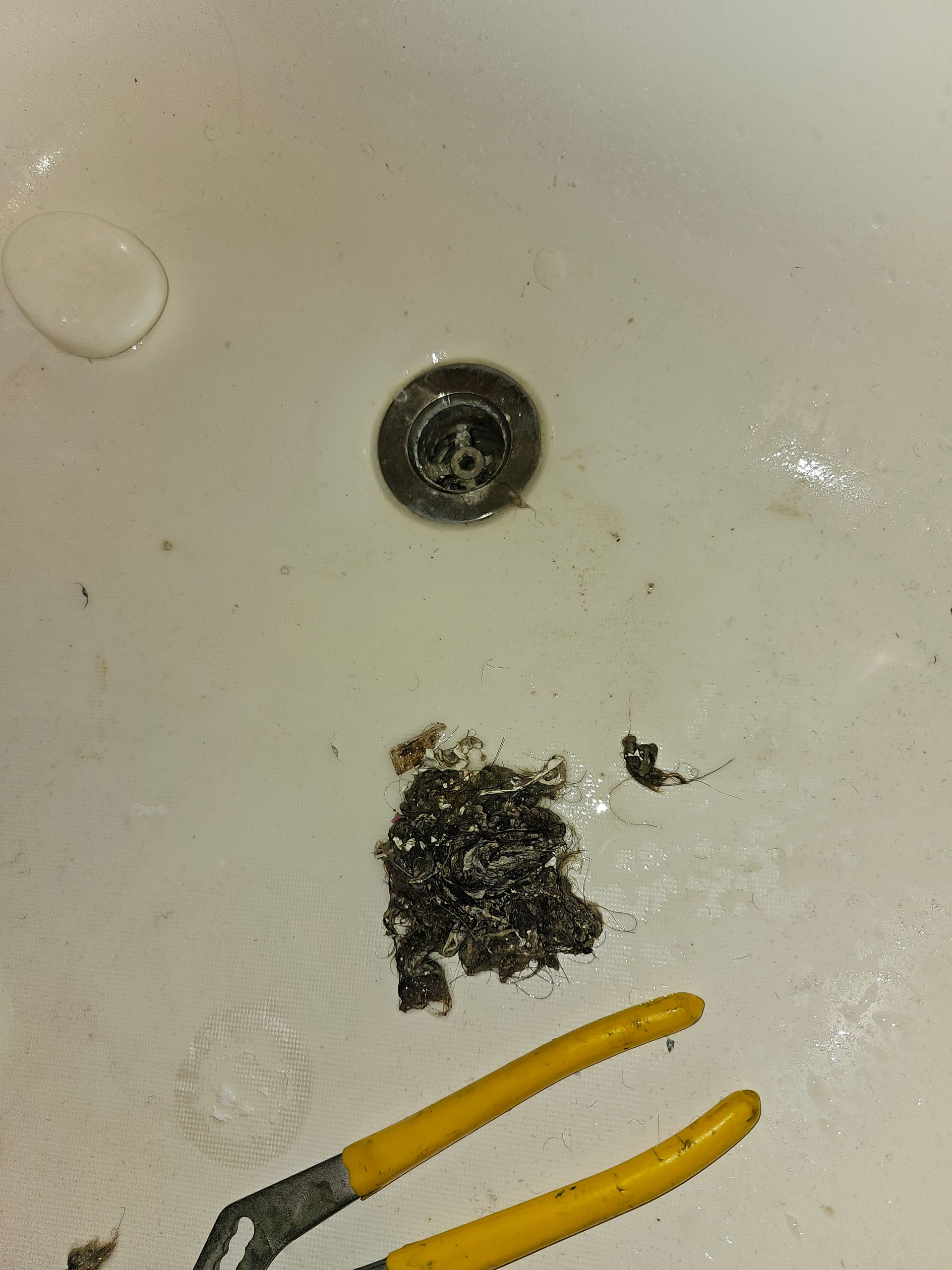 Hair clog pulled from a bathtub drain next to yellow-handled pliers.