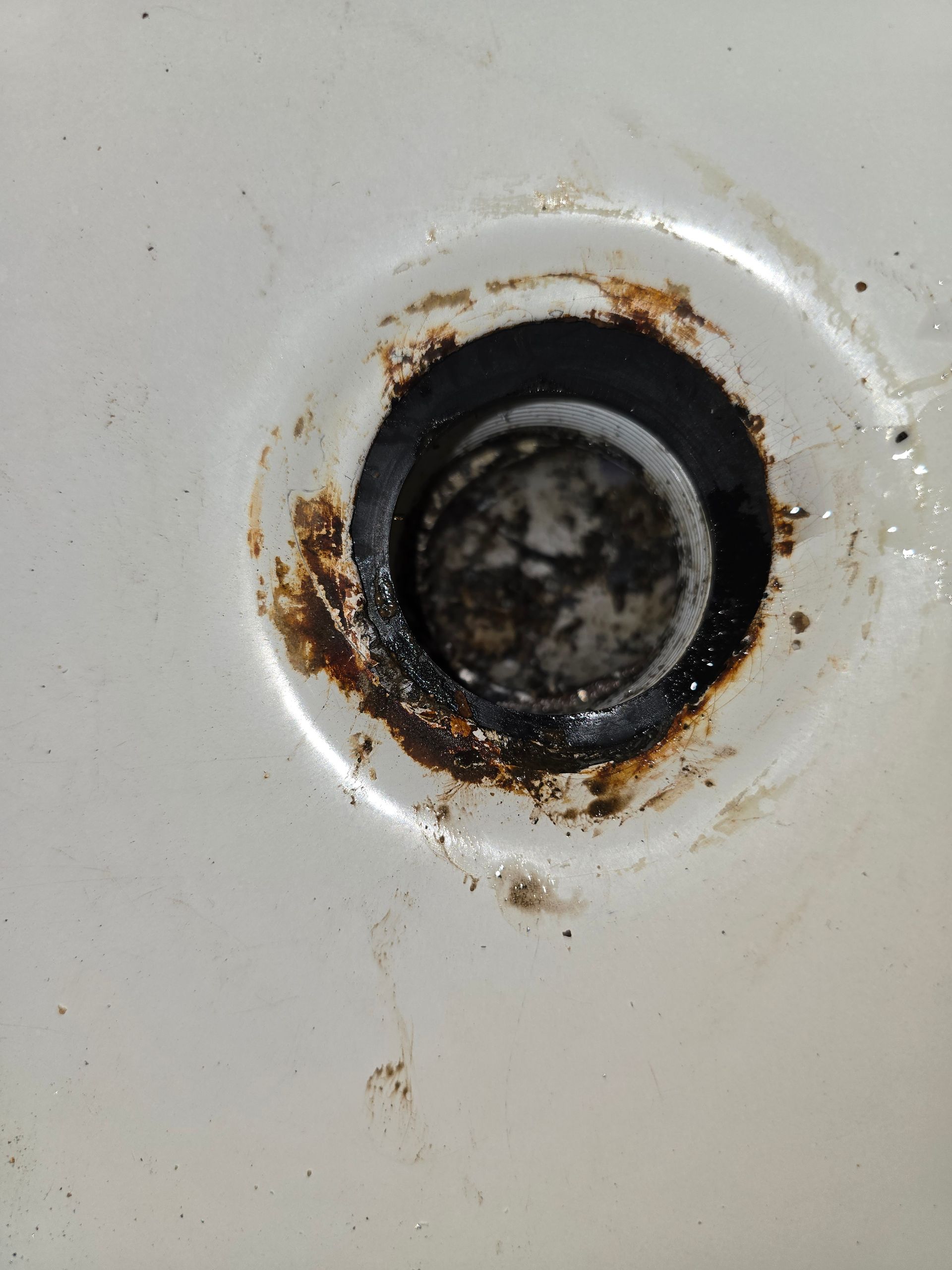 Close-up of a dirty bathtub drain with dark gunk and rust around the edge, white tub.