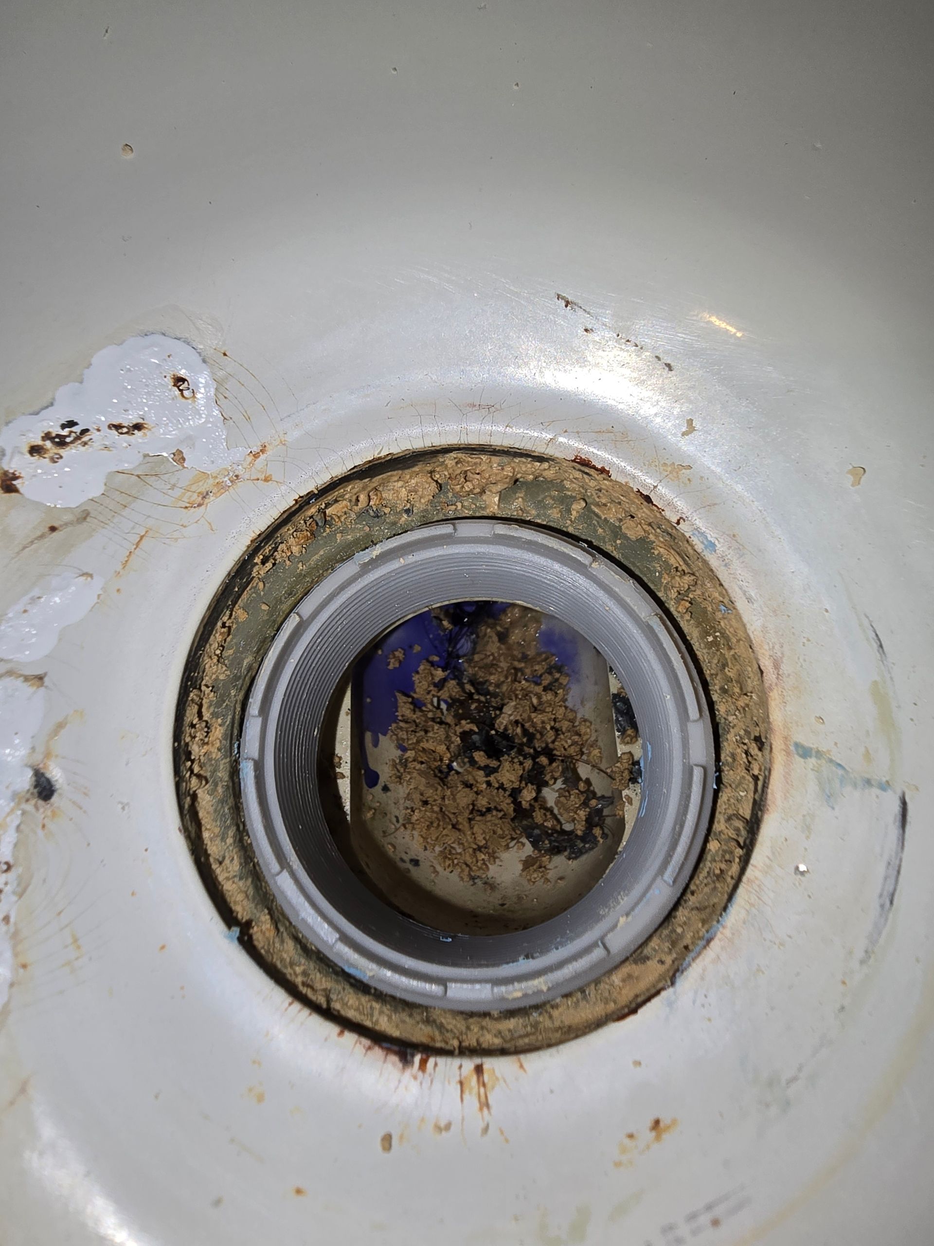 Dirty sink drain with a clogged strainer, surrounded by rust and debris.