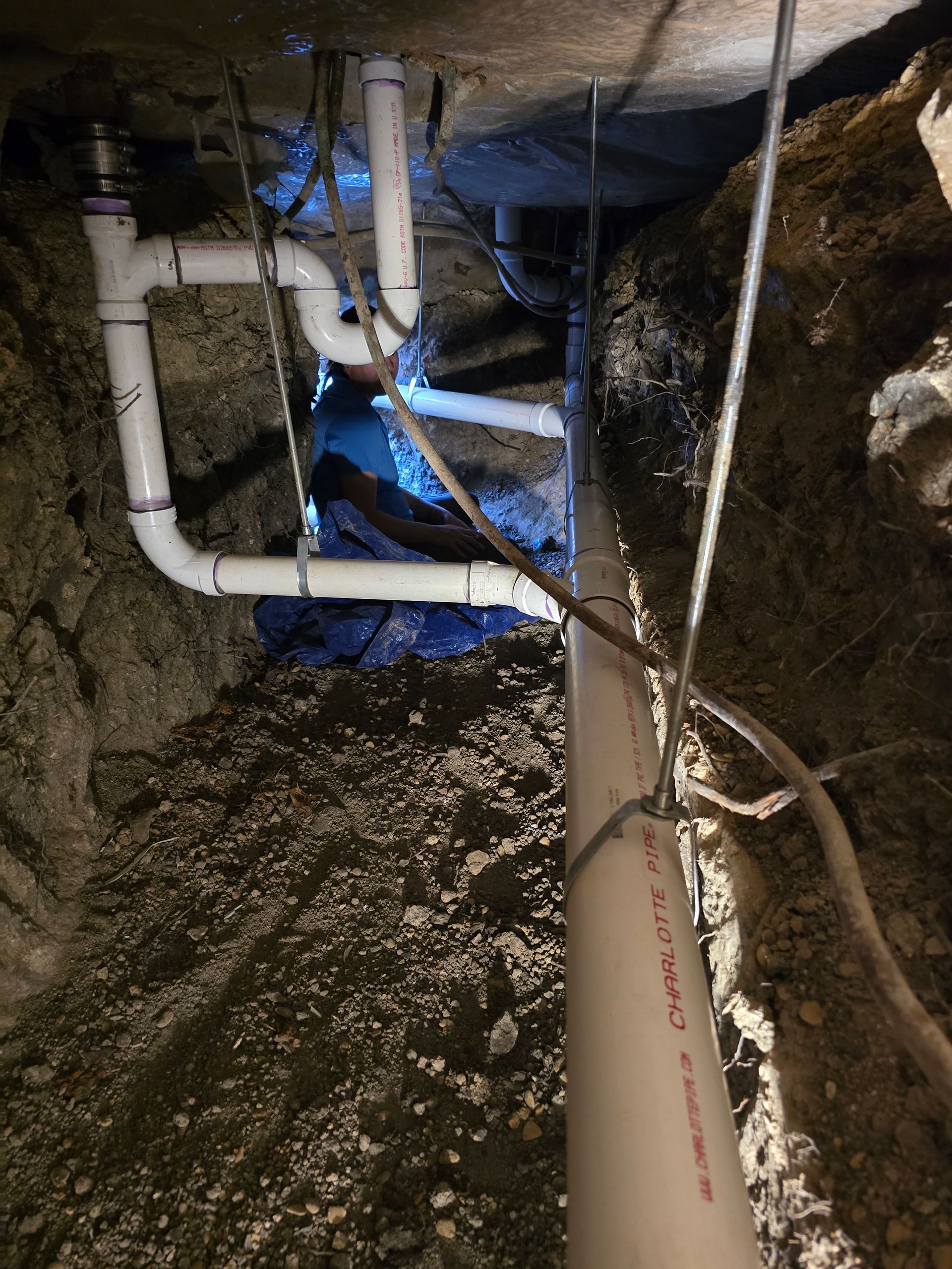 White PVC pipes in a dark trench, likely for plumbing. Vertical view.