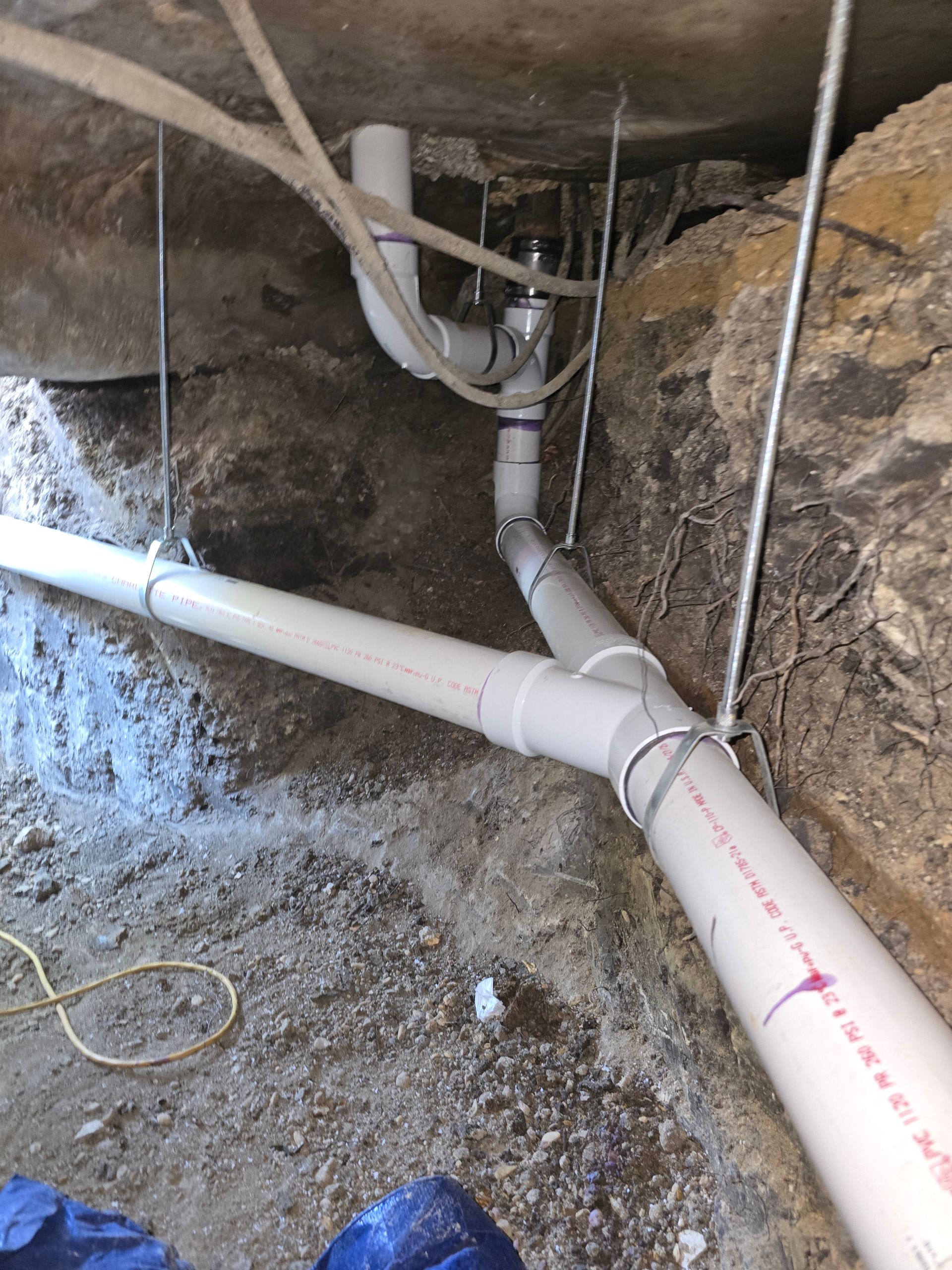 PVC plumbing pipes installed in a basement, angled and supported against a stone wall.