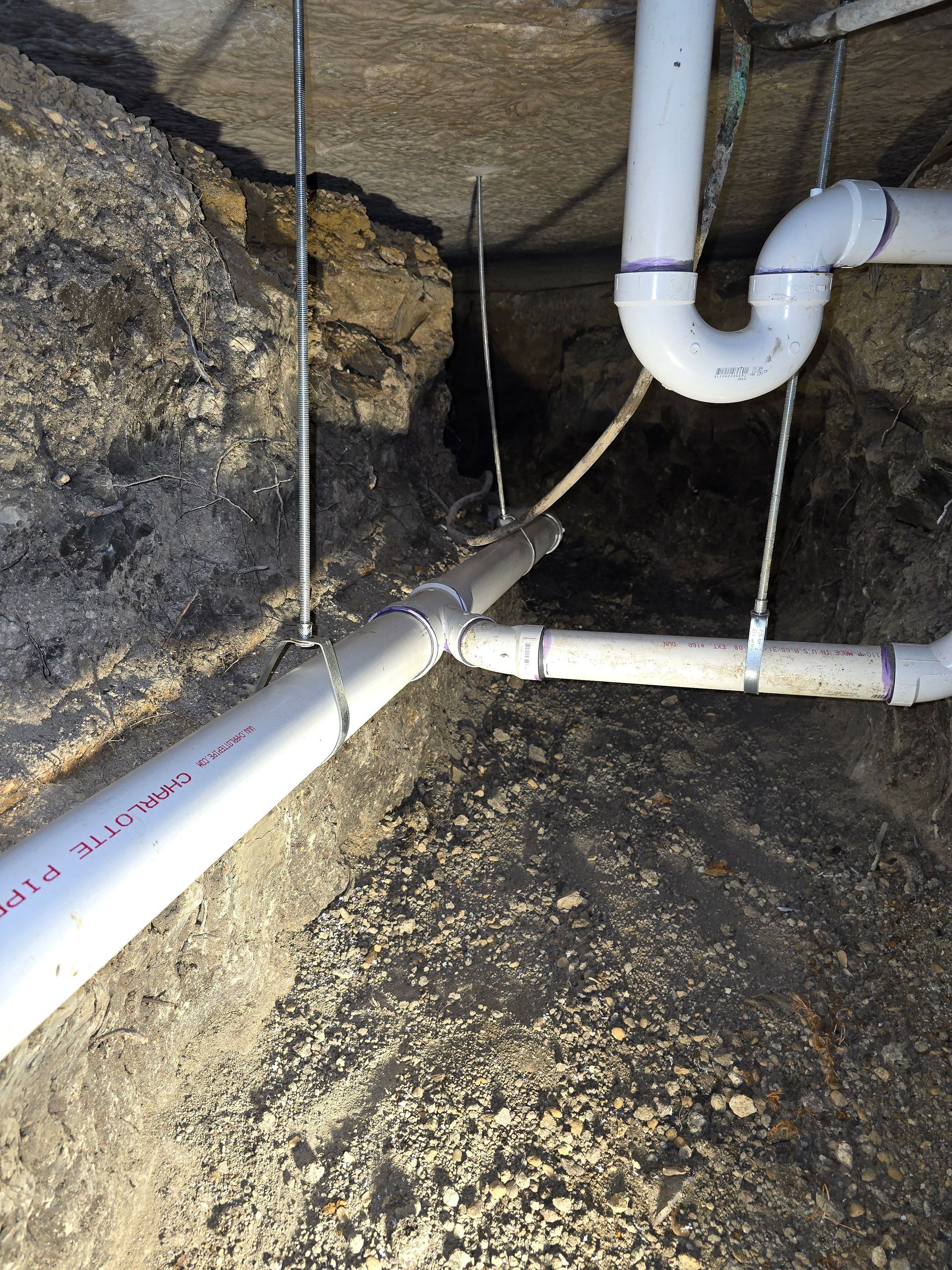 PVC plumbing pipes installed in an unfinished basement, secured with metal rods.