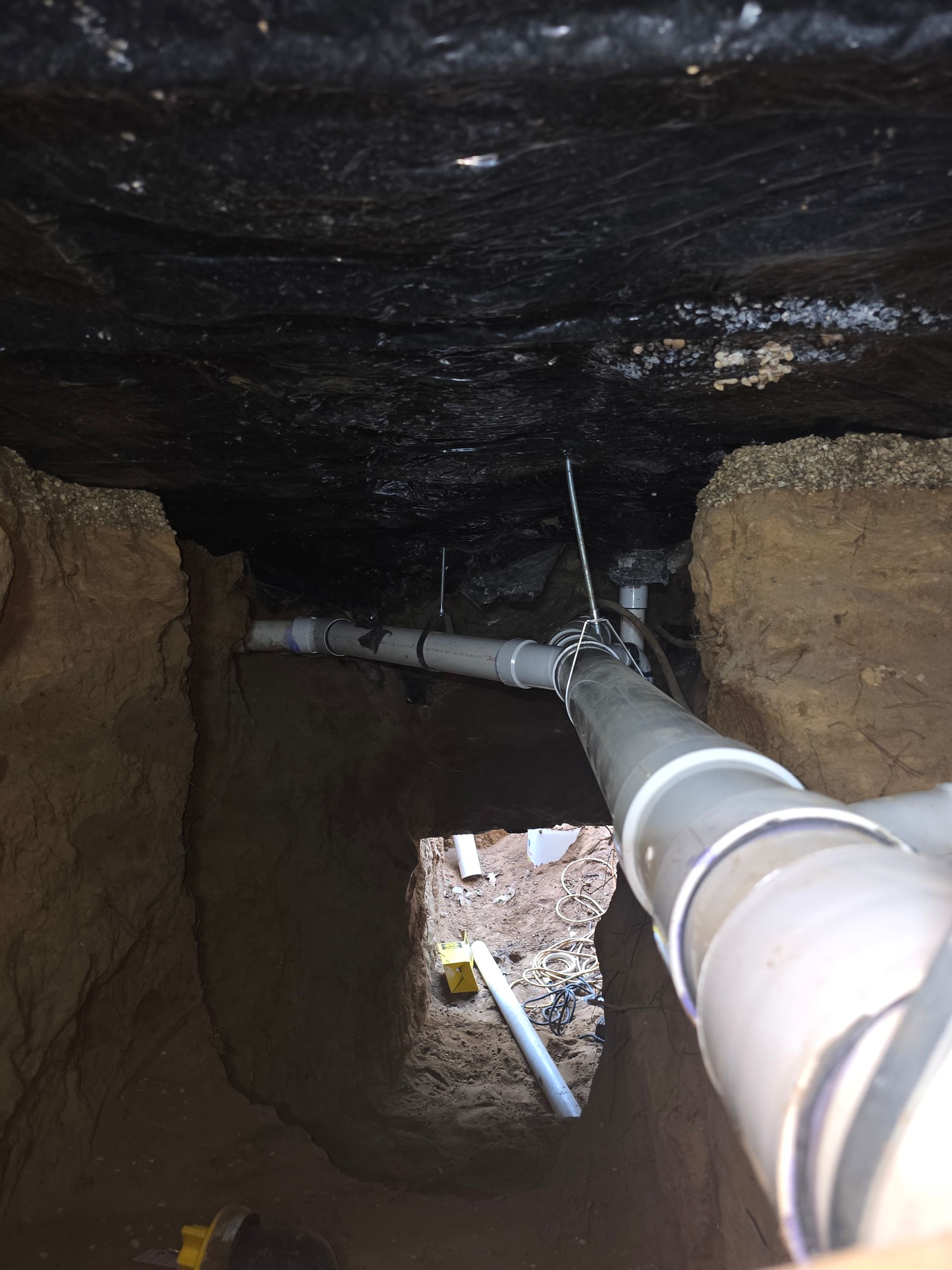Pipes and fittings in a trench under a dark surface.