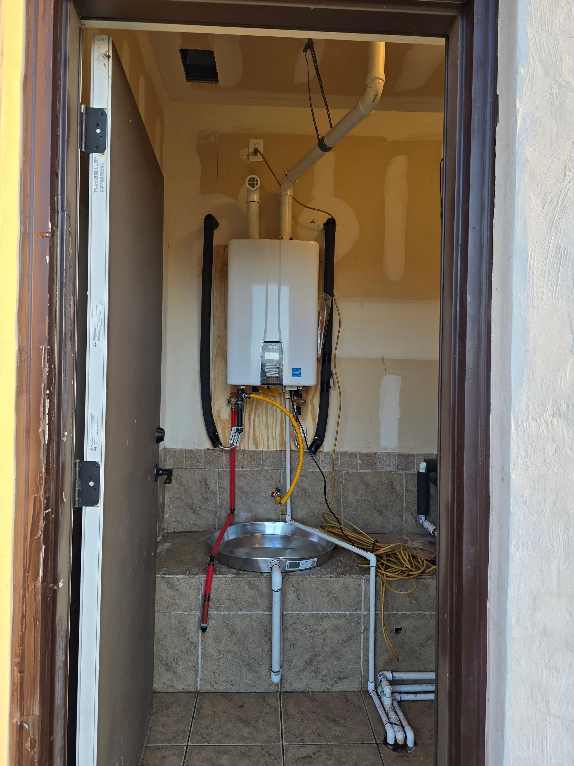 View of an outdoor sink area. A water heater is mounted above the sink with exposed plumbing.