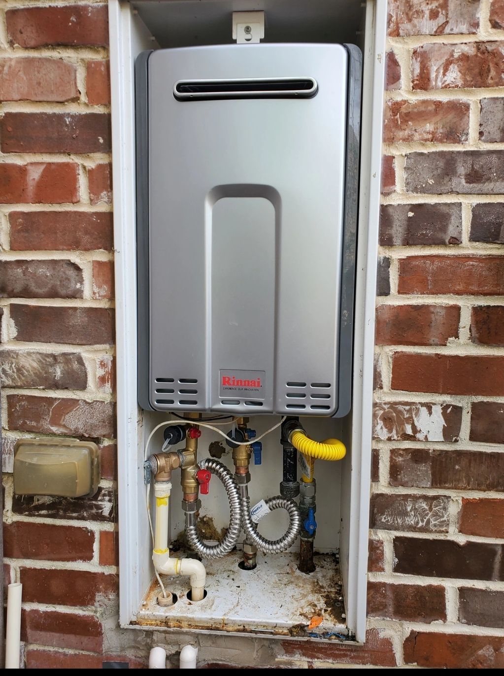 A tankless water heater mounted in a brick wall alcove.