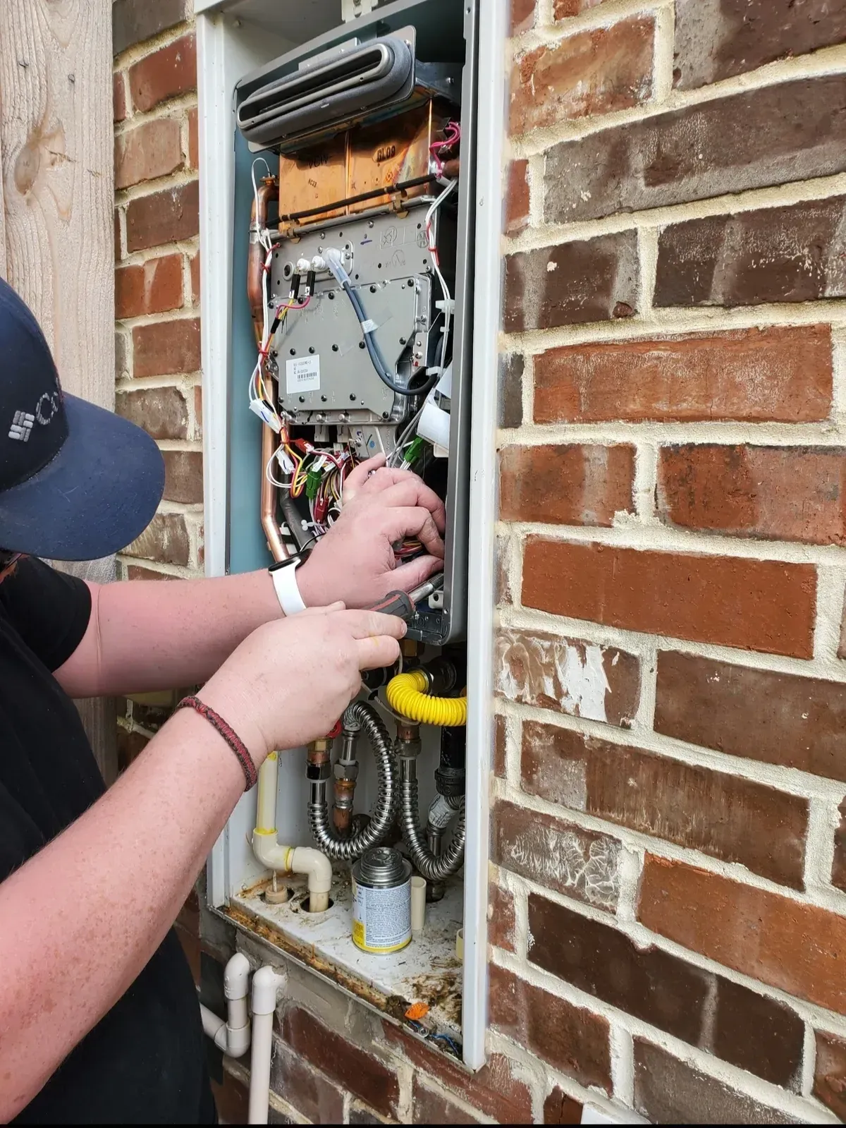 A person works on a tankless water heater installed in a brick wall.