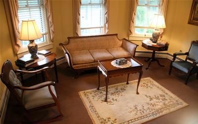 Cozy vintage living room with beige sofa, two armchairs, wooden tables, lamps, and a floral rug near windows