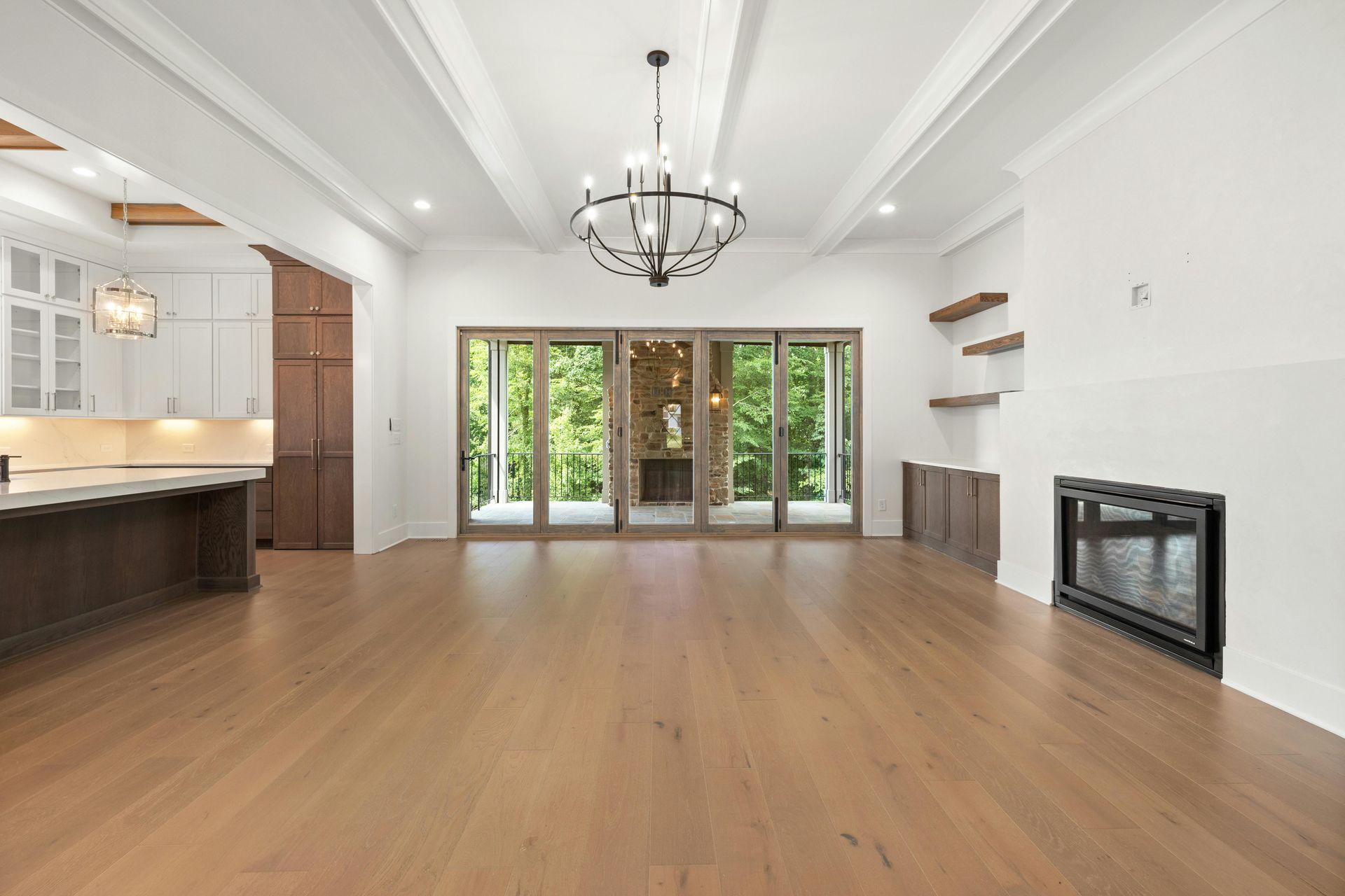 A painter in white clothing stands on a wooden ladder, painting a large gray wall in a sunlit room.