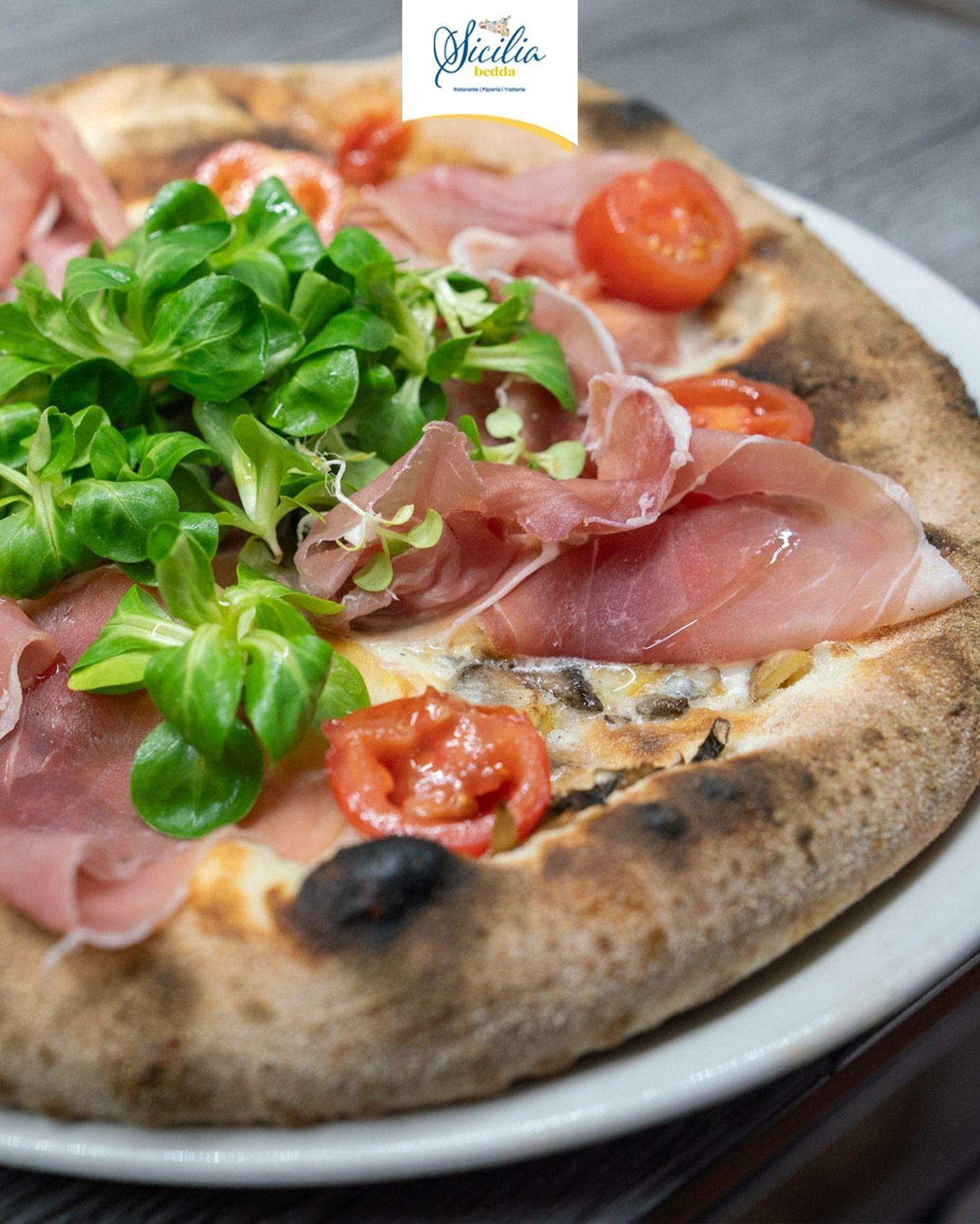 Pizza con prosciutto crudo, verdure fresche e pomodorini ciliegino su un piatto bianco