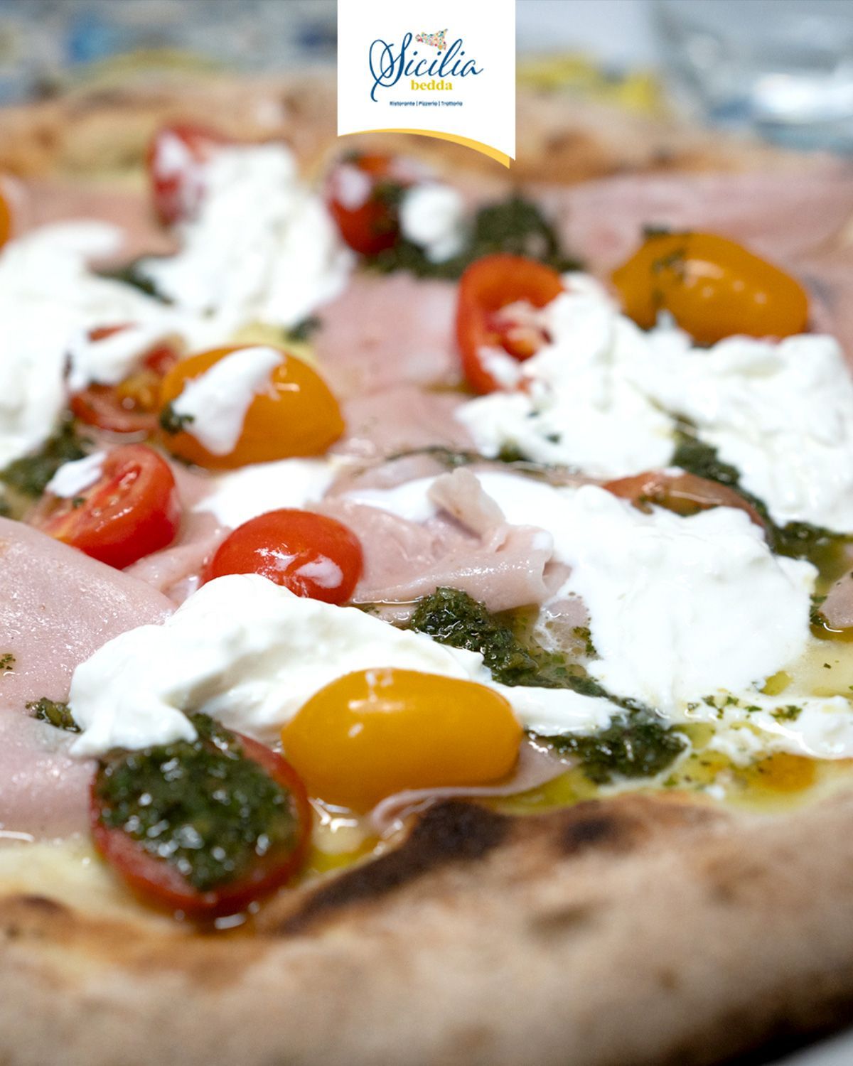 Primo piano di una pizza con pomodorini, formaggio fuso, basilico e prosciutto
