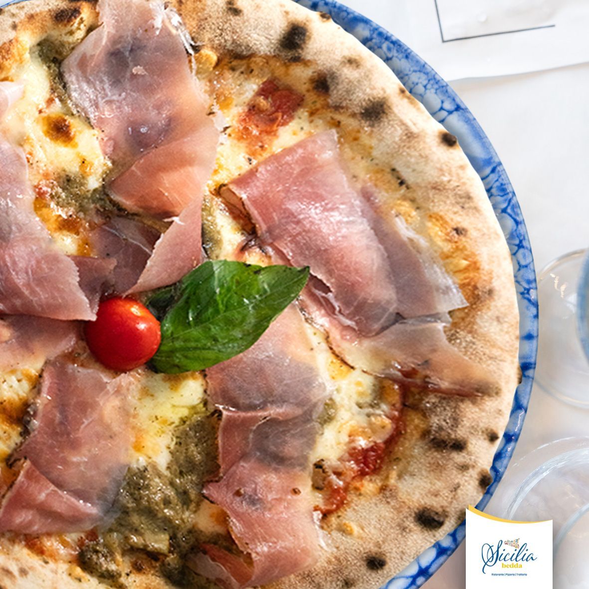 Pizza condita con prosciutto crudo, basilico, pomodoro e mozzarella