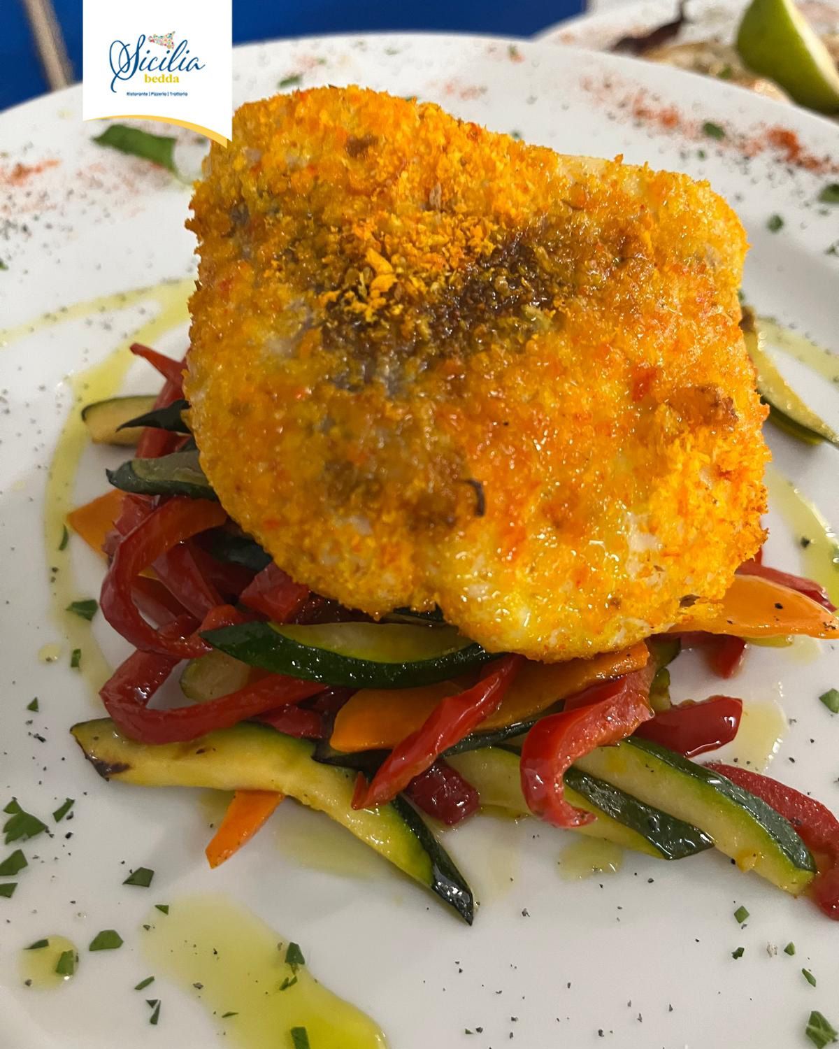 Filetto di pesce dorato impanato su un piatto bianco con peperoni e verdure saltate.