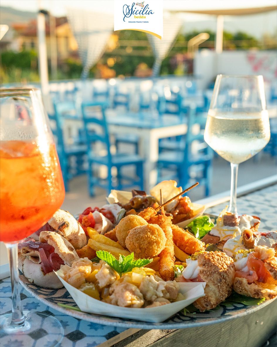 Cocktail e vino accanto a un piatto di antipasti su un tavolo da patio all'aperto con sedie blu.