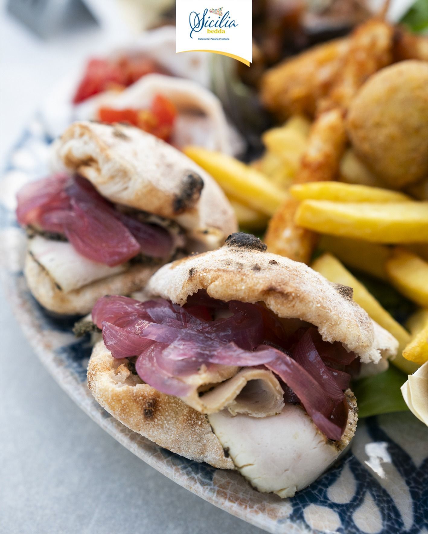 Due piccoli panini con pane piatto, carne e cipolle, accompagnati da patatine fritte, su un piatto decorato.