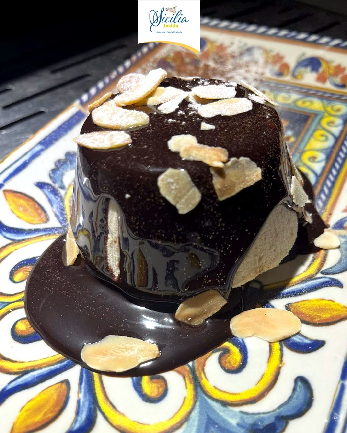 Torta al cioccolato fondente con cuore caldo e scaglie di mandorle, servita su un piatto decorativo blu e giallo.