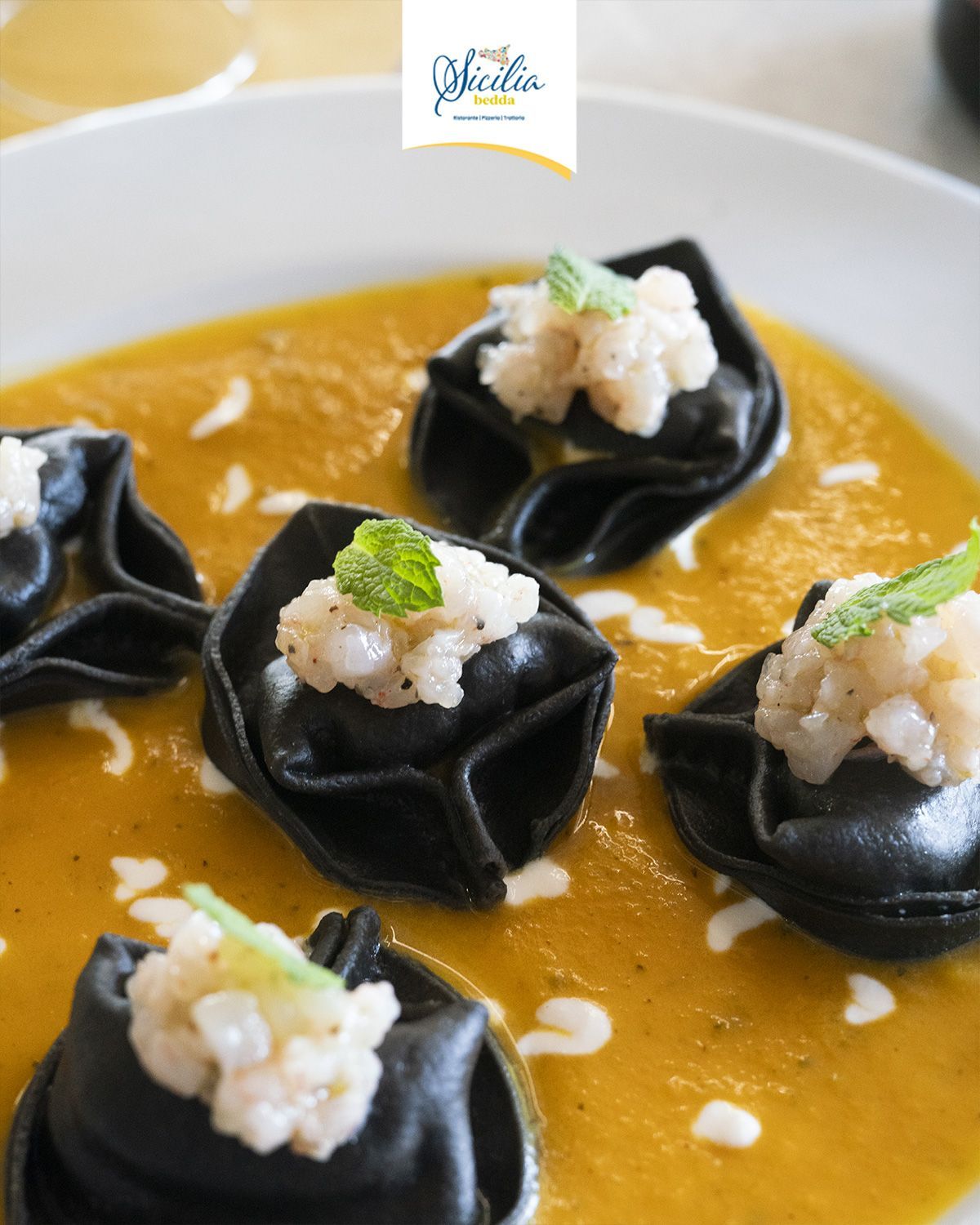 Ravioli neri con ripieno bianco e guarnizione verde in salsa arancione su un piatto bianco.
