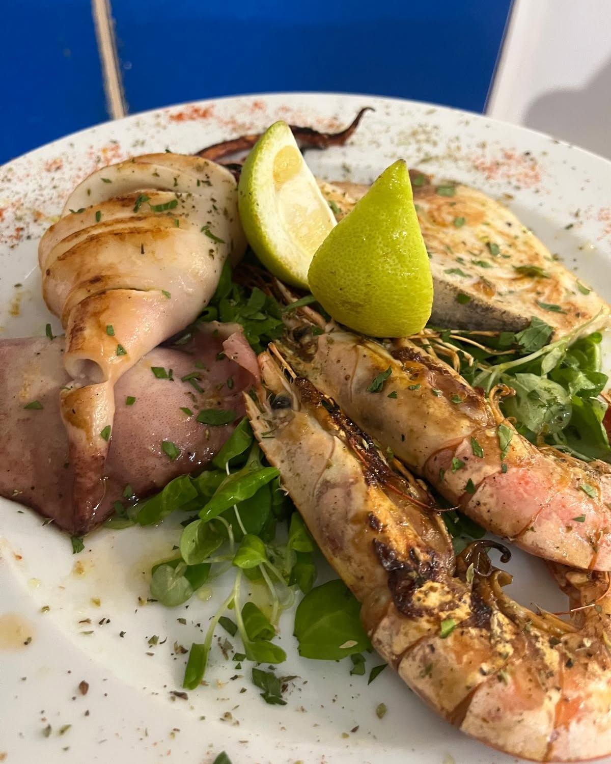 Piatto di frutti di mare grigliati con gamberi, capesante, verdure e spicchi di lime su un piatto bianco.