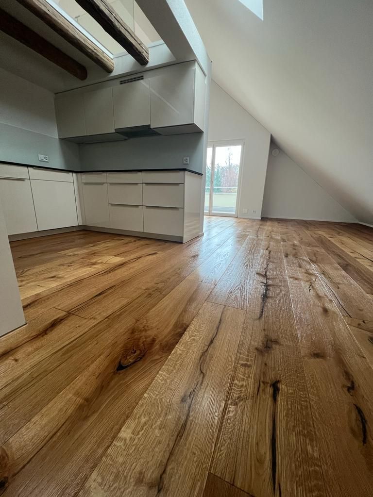 Holzboden in einem Dachzimmer mit weißen Schränken und einer Tür nach draußen.