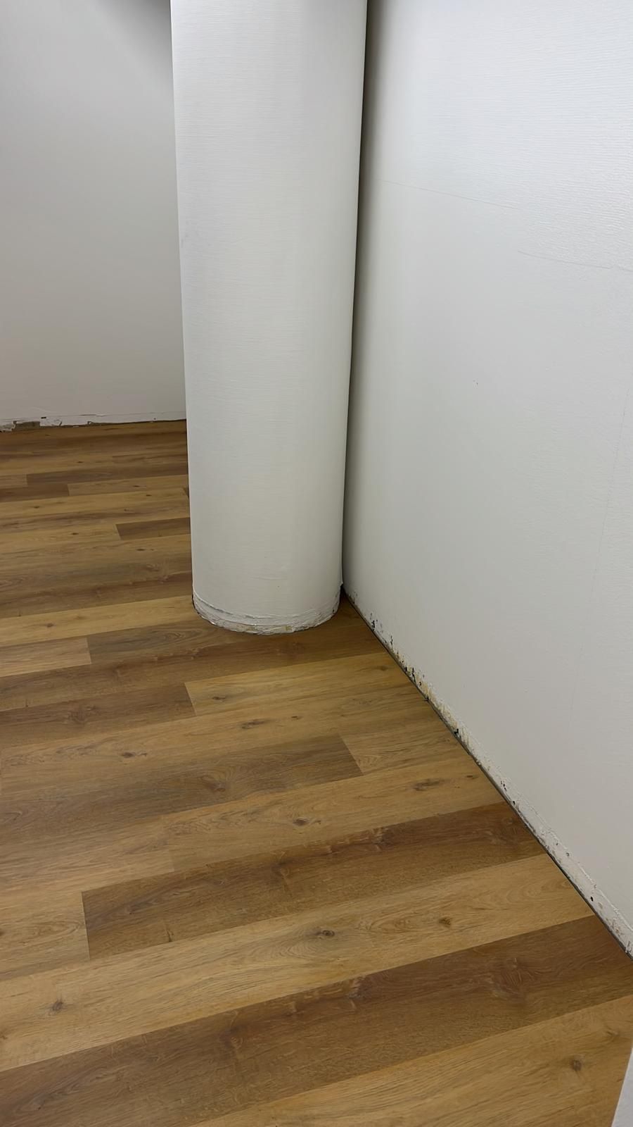 Holzboden mit einer weißen Säule neben einer weißen Wand.