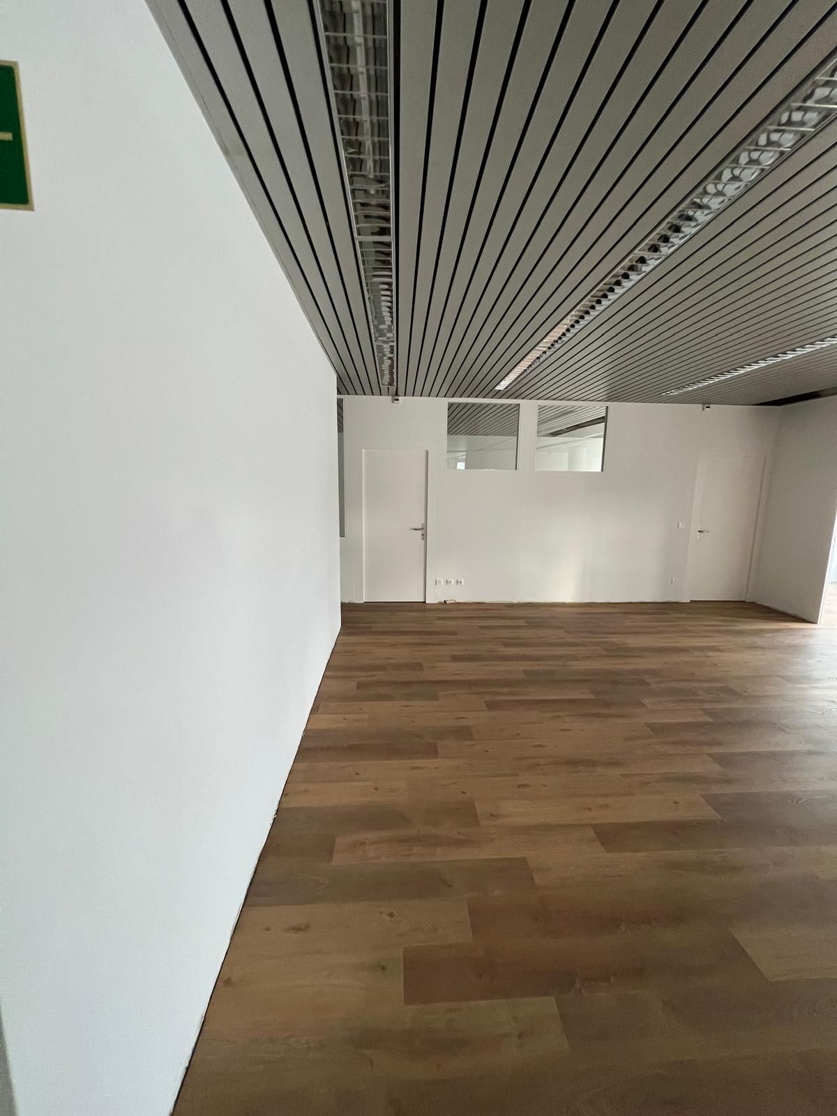 Leerer Raum mit Holzbodenoptik, weißen Wänden und strukturierter Decke.