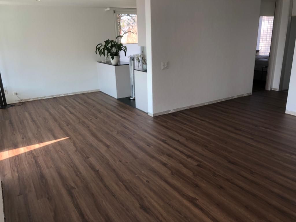 Leeres Zimmer mit dunklem Holzboden, weißen Wänden und einer kleinen Topfpflanze auf der Theke.