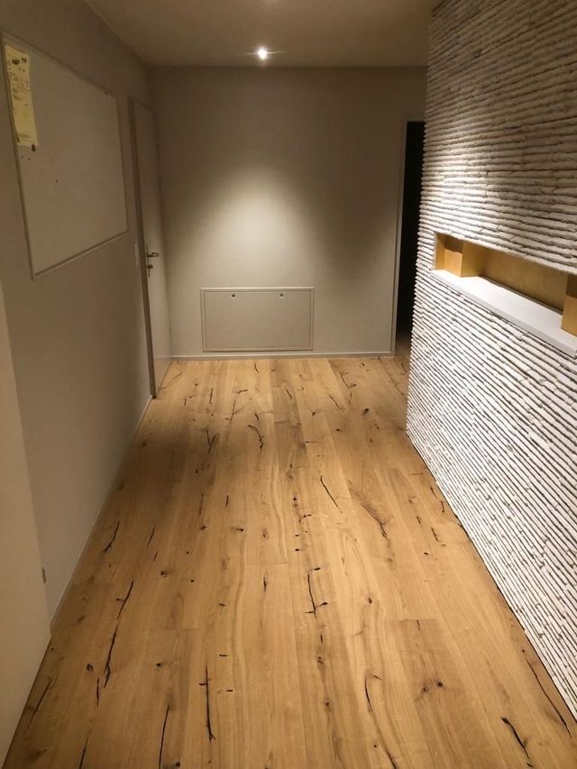 Holzflur mit strukturierter weißer Wand, eingebauten Regalen und einer weißen Tür.
