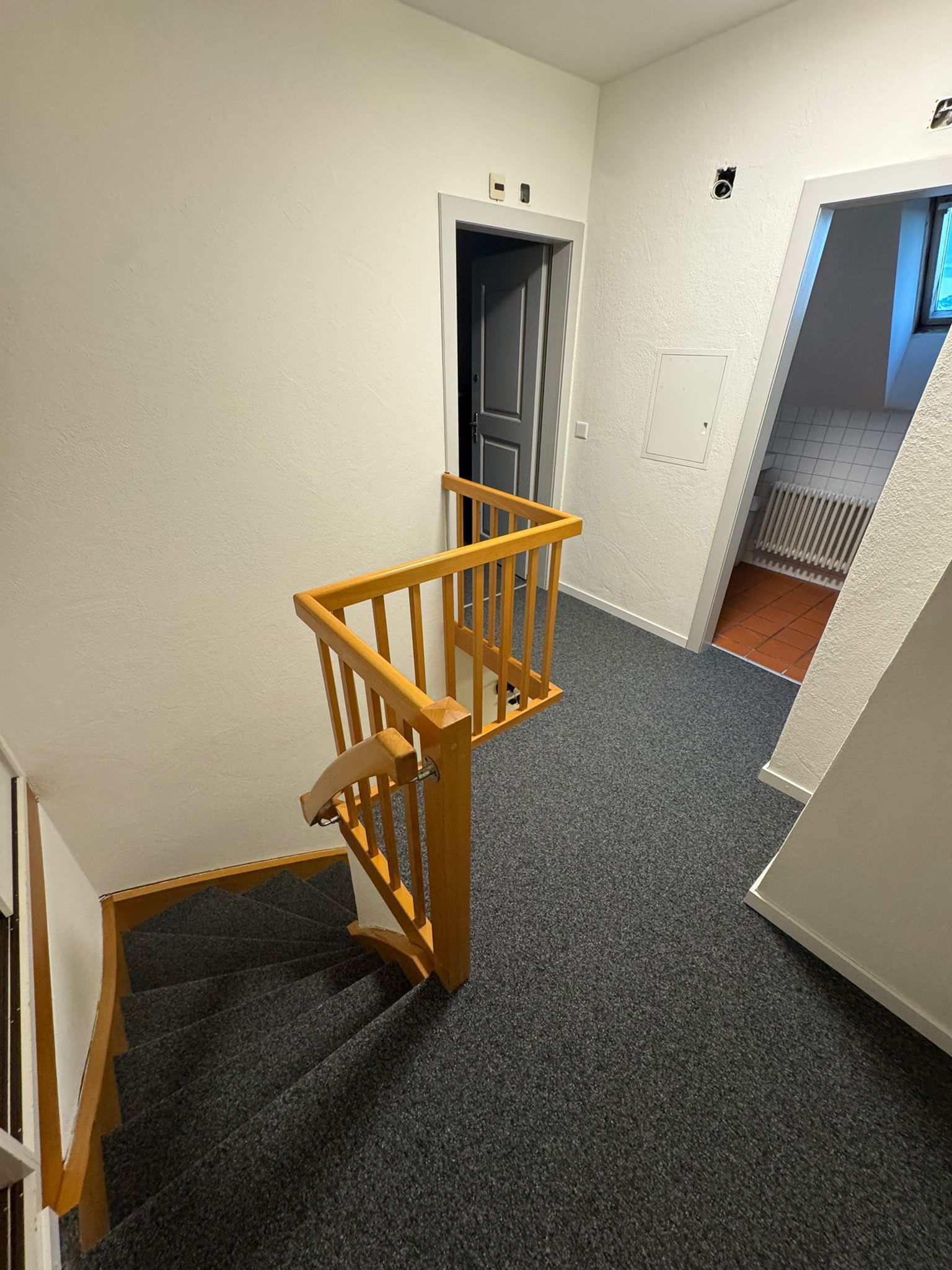 Treppe mit Holzgeländer und Tür auf dem Treppenabsatz, grauer Teppich.