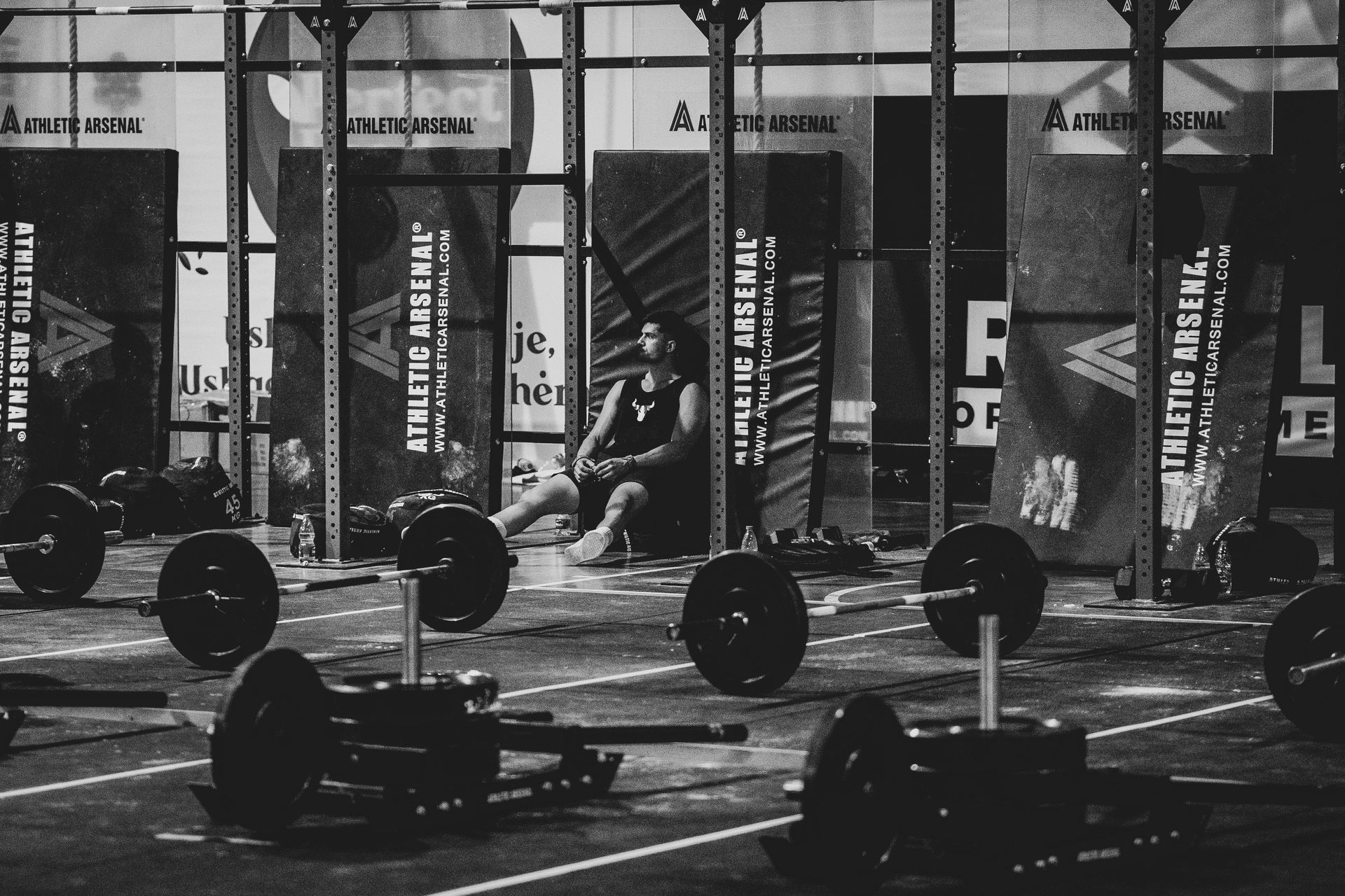 Black-and-white gym with barbells on the floor and a person lifting in the background