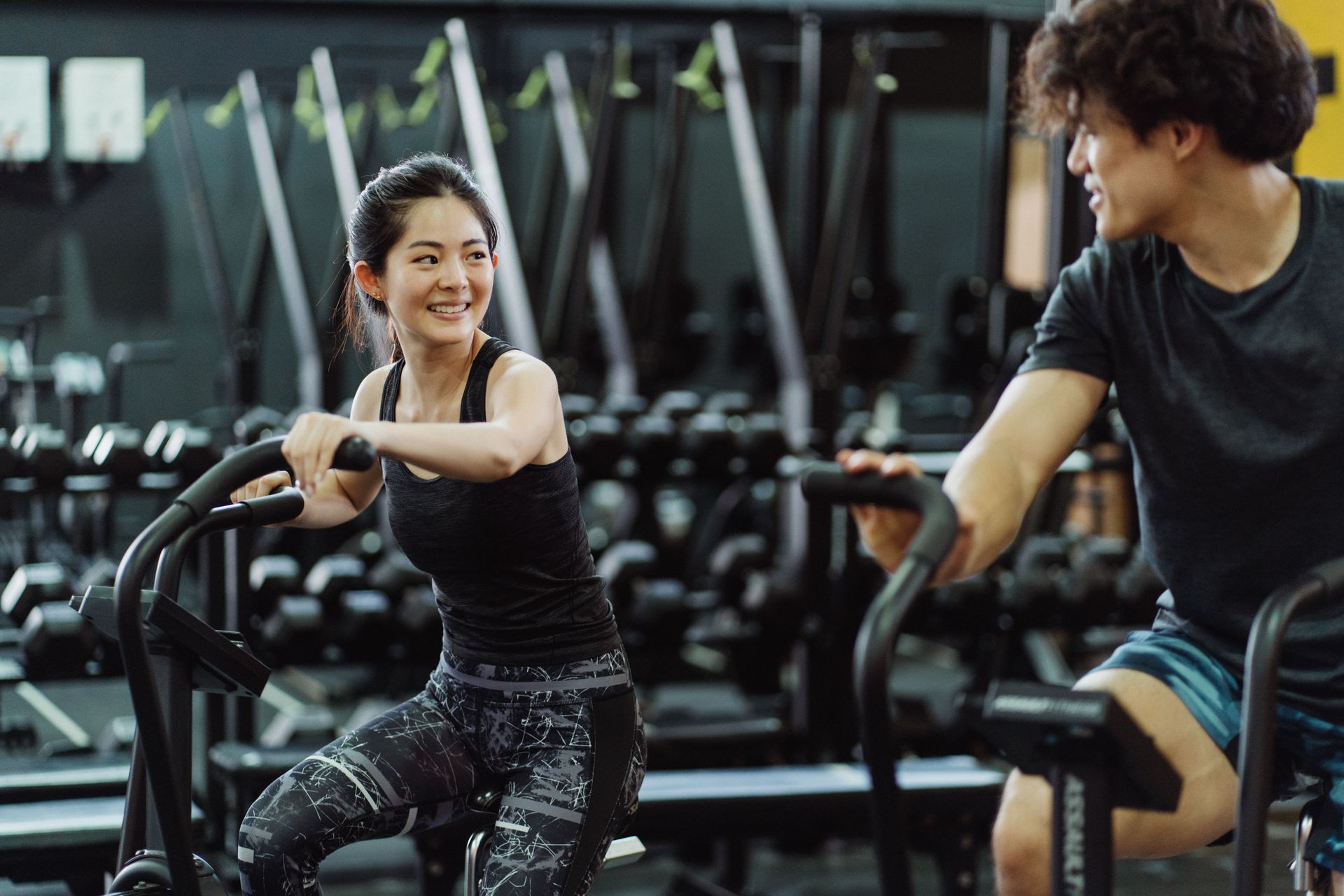 Two people chatting while exercising on stationary bikes in a gym