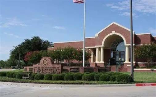 A brick building with an arched entrance, a flagpole, and a sign reading "District" surrounded by trimmed hedges.