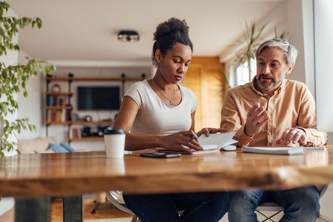 Two people reviewing papers at a dining table in a warm, sunlit kitchen